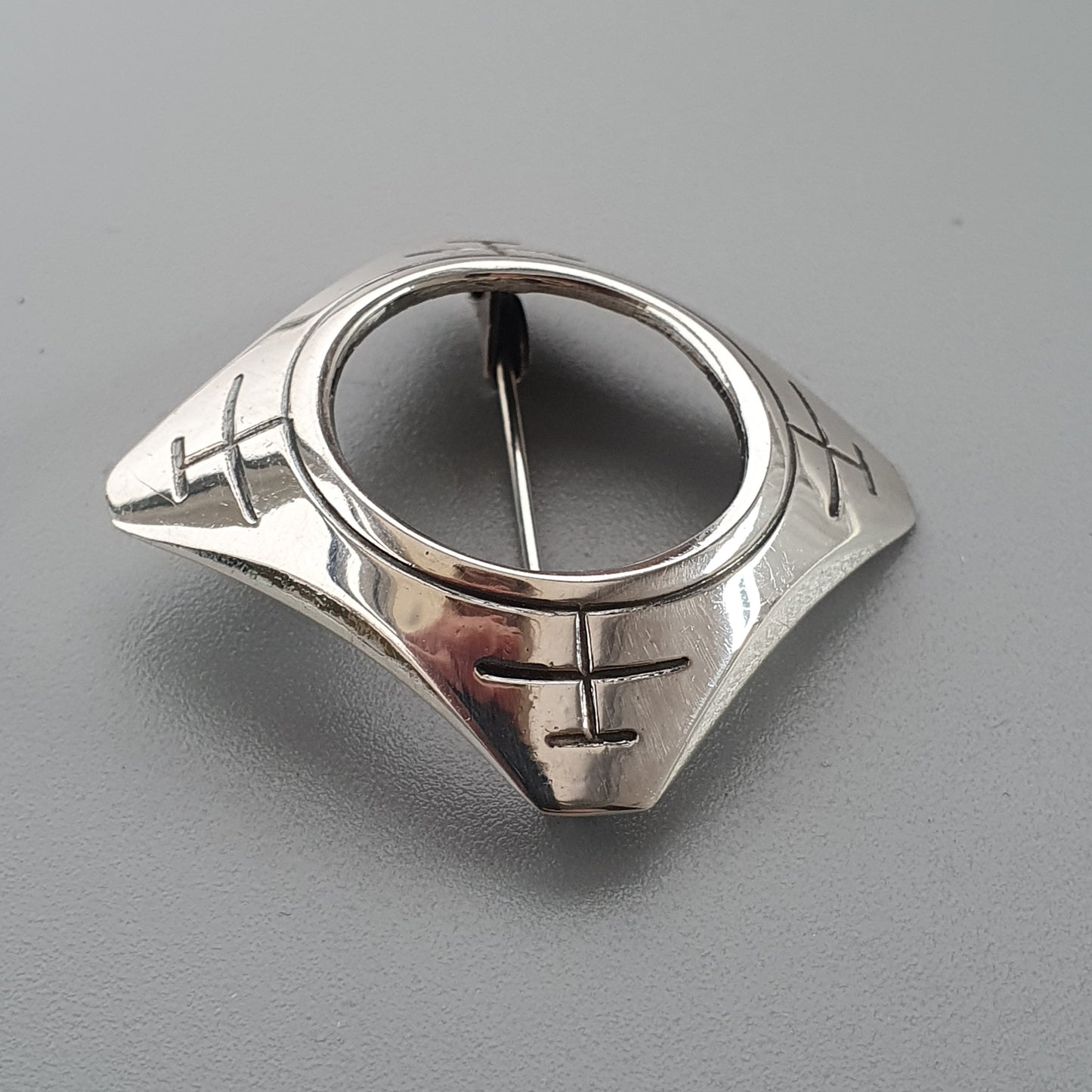 Silver ring with a circular black face and geometric designs on the band.