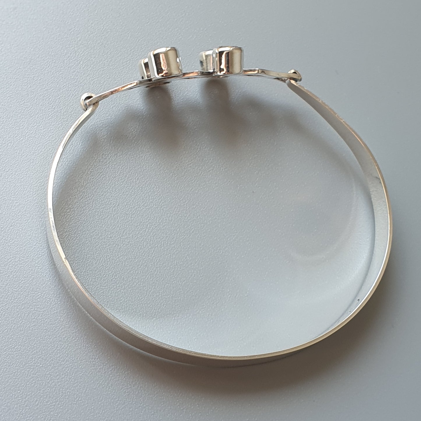 Silver bangle bracelet with two small cylindrical attachments.
