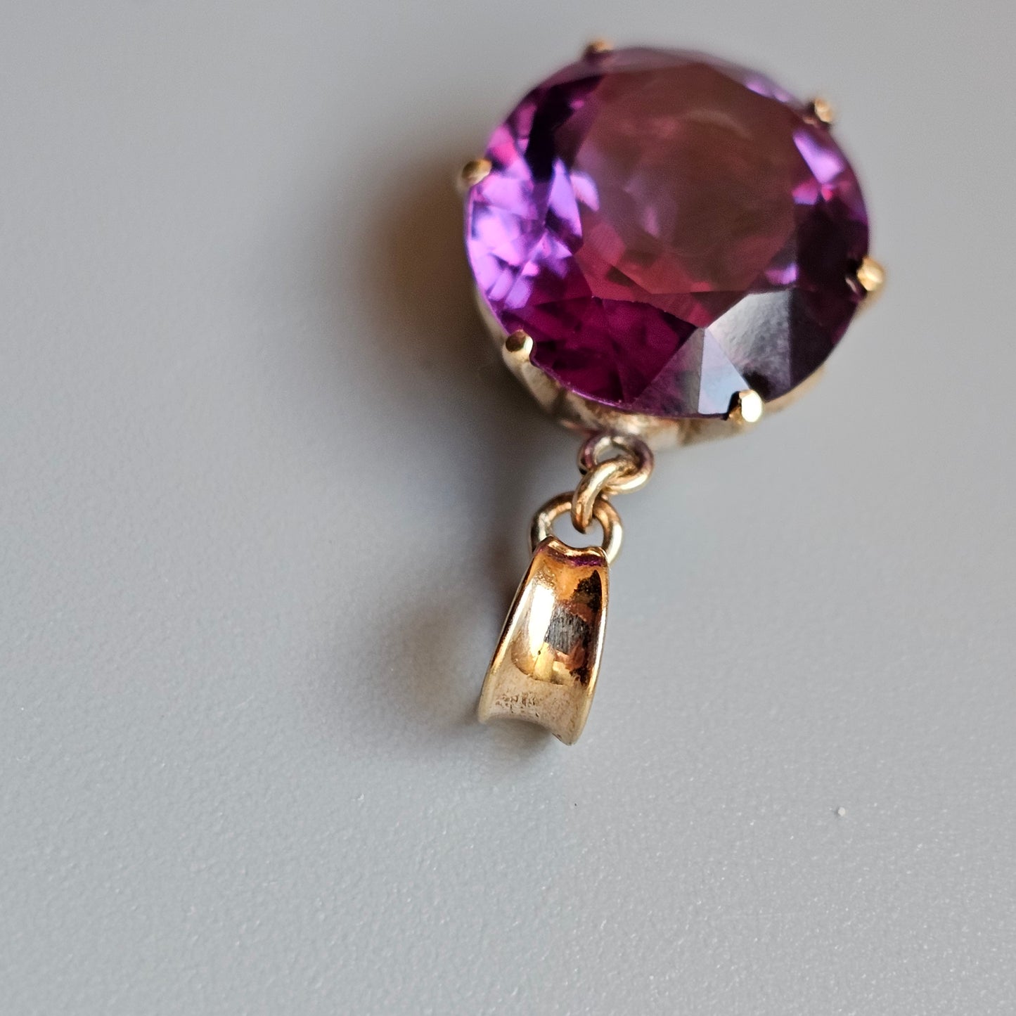 Faceted purple gemstone pendant with a gold-colored clasp.