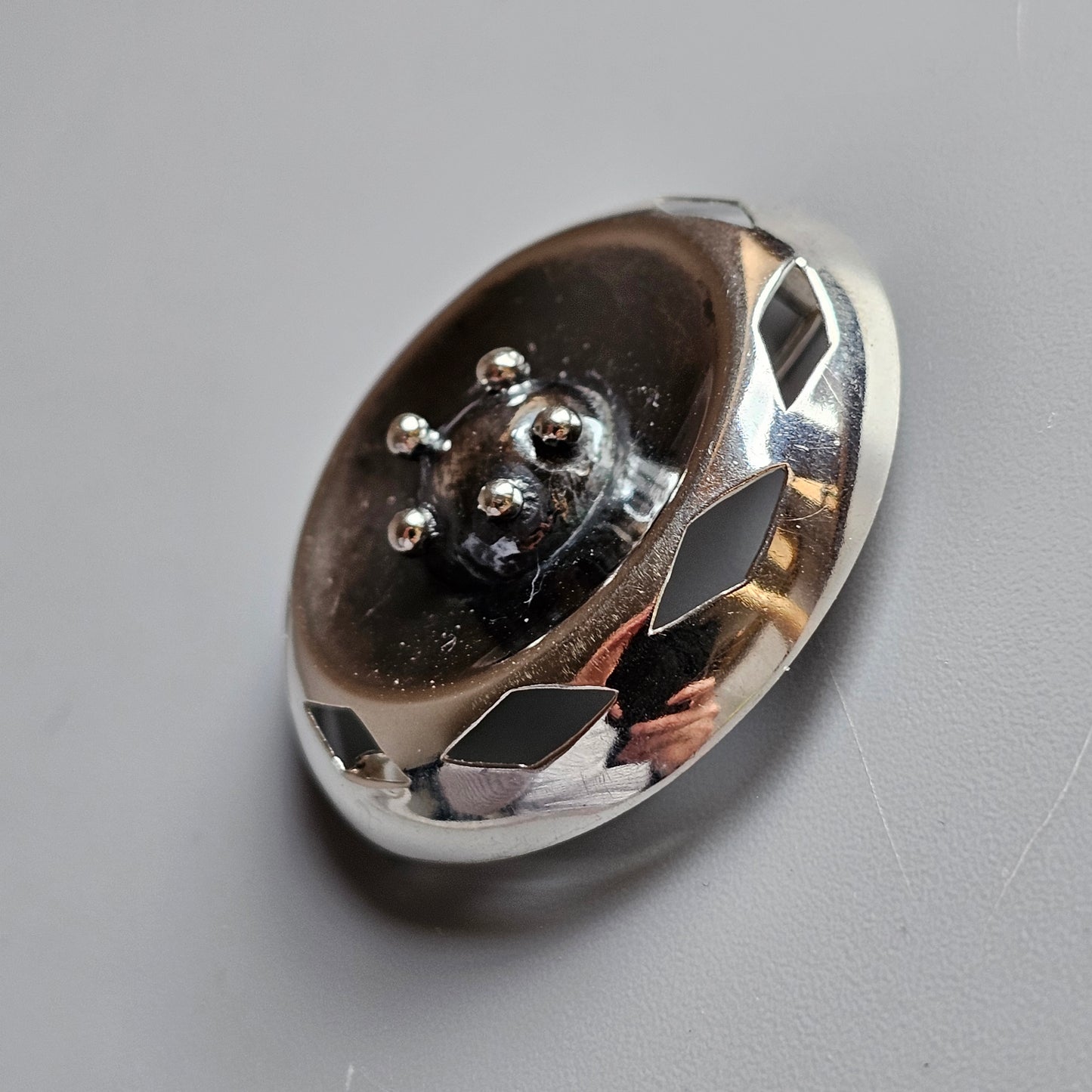 Oval-shaped silver brooch or pendant with a raised floral design on its surface.