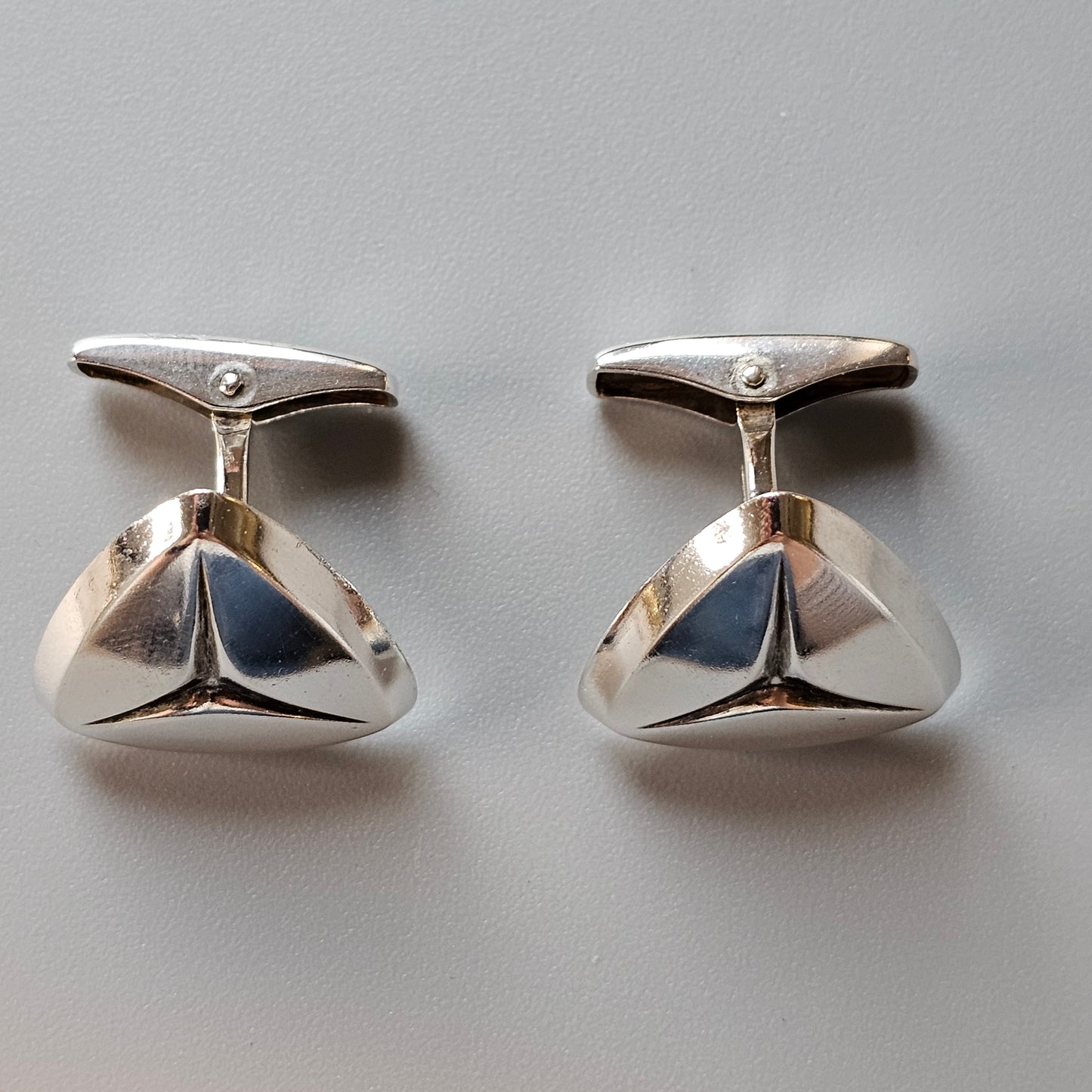 Pair of silver cufflinks with a triangular, three-lobed design.