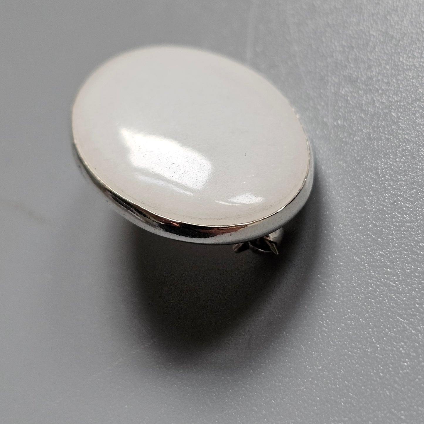 Oval-shaped, pearlescent button or decorative element with a metallic rim.