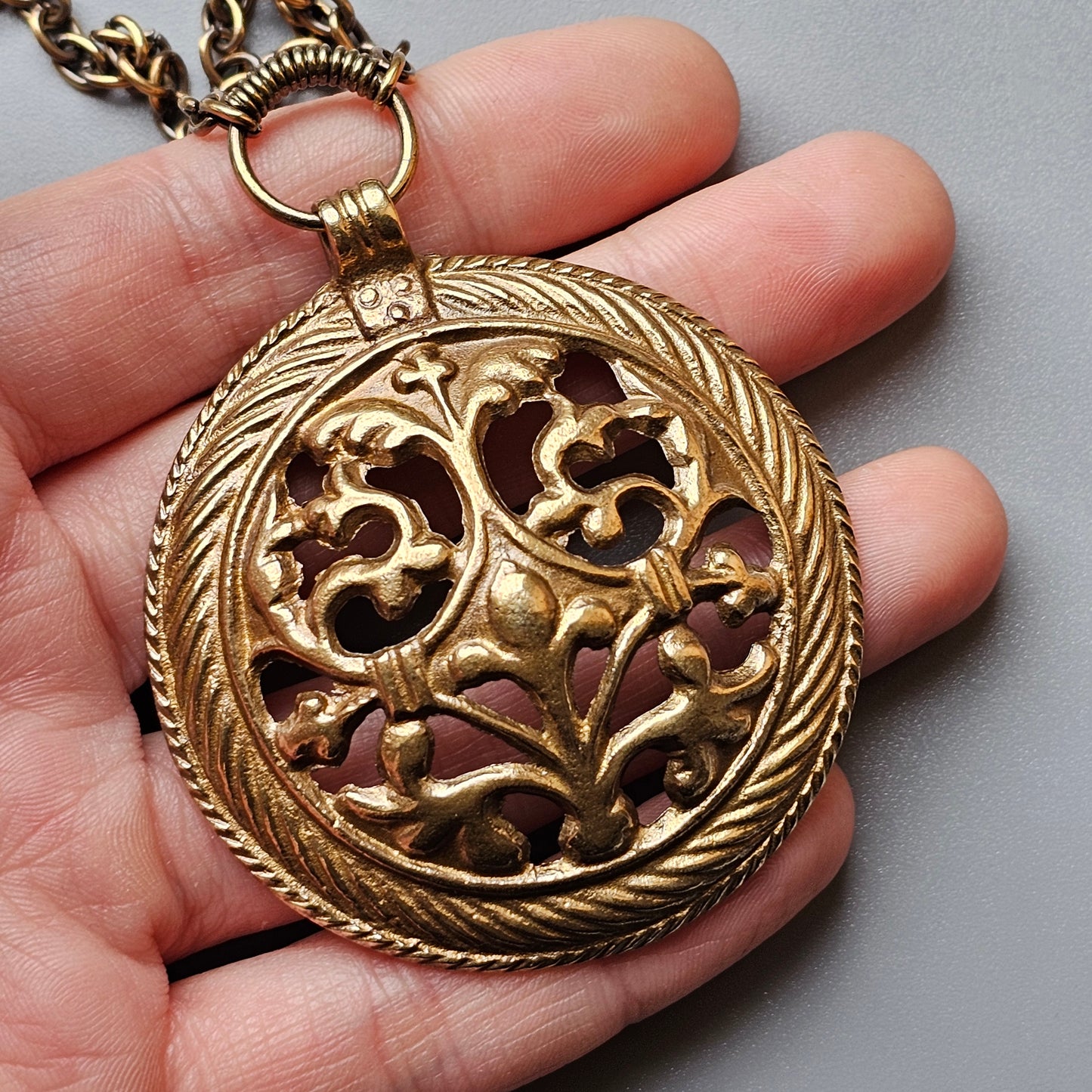 Ornate gold medallion pendant with intricate filigree design held in a person’s palm.