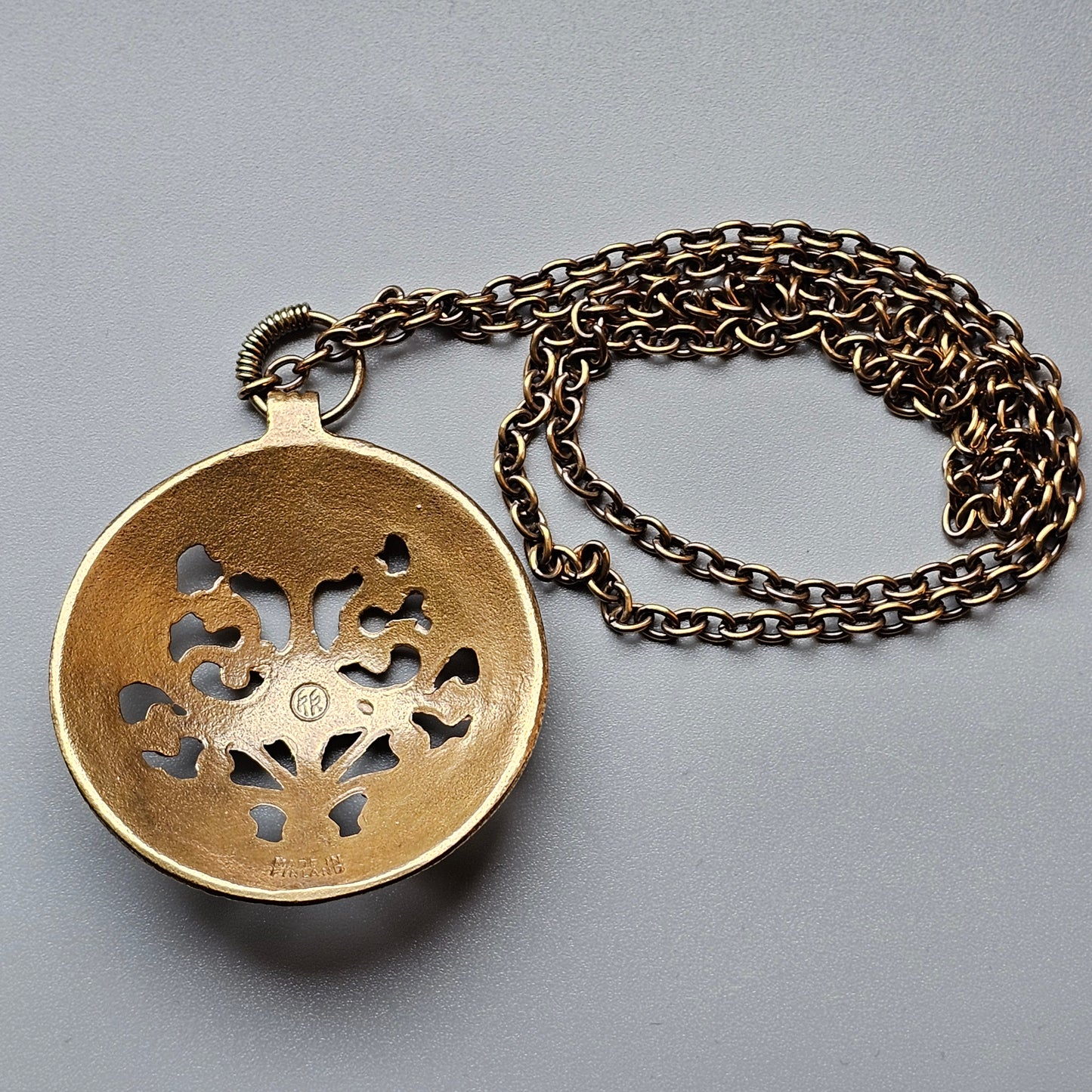 Ornate gold-colored pendant with intricate cutout design on a metal chain.