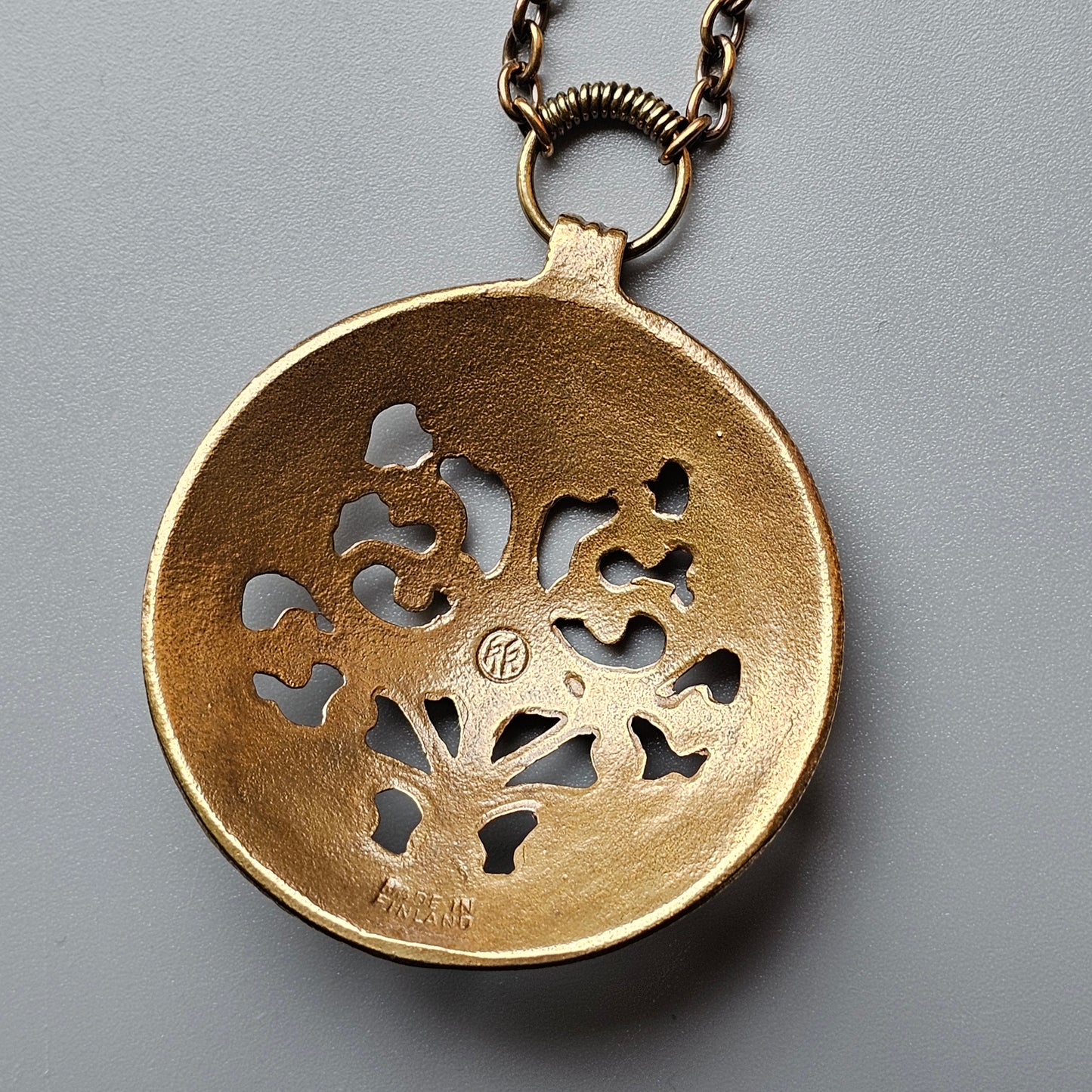 Gold-colored pendant necklace with a circular design featuring cutout tree-like patterns.