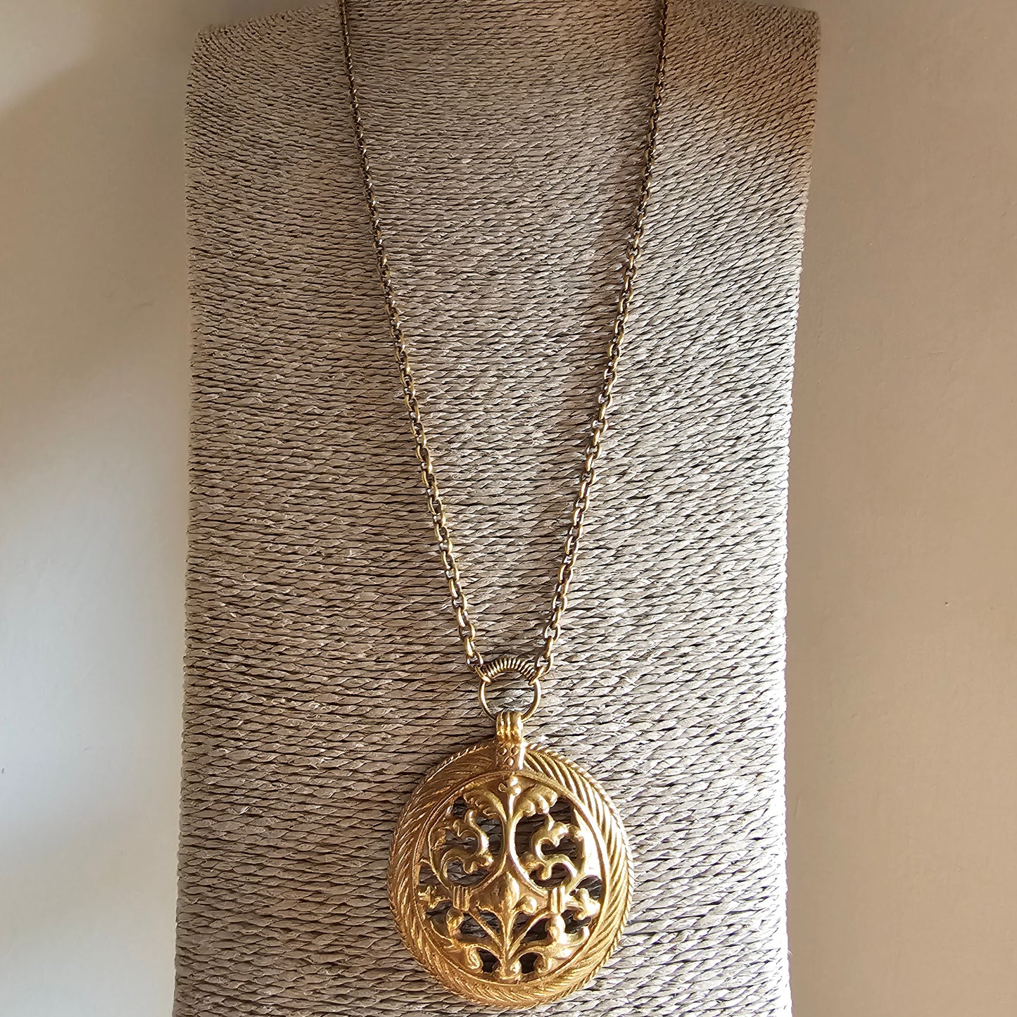 Gold-toned ornate locket pendant on a chain necklace.