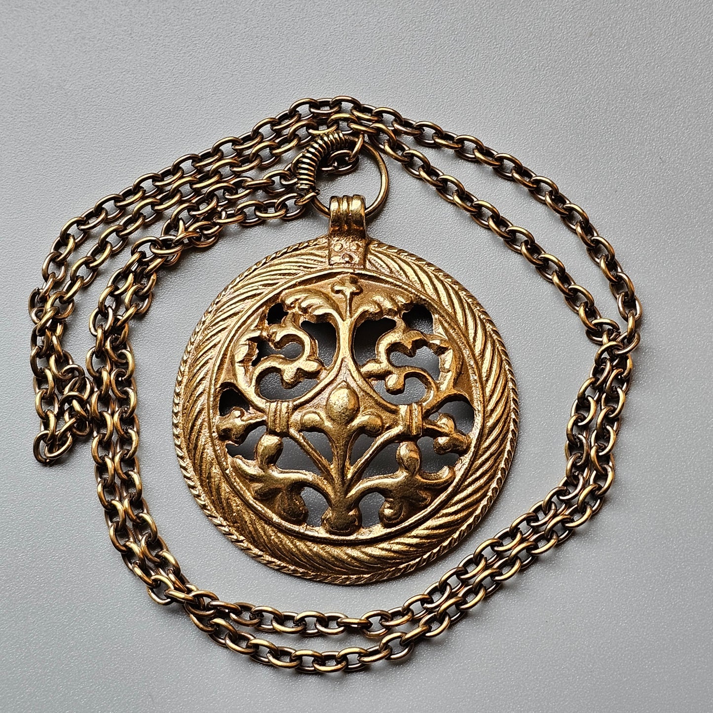 Ornate gold pendant with intricate floral filigree design on a chain necklace.