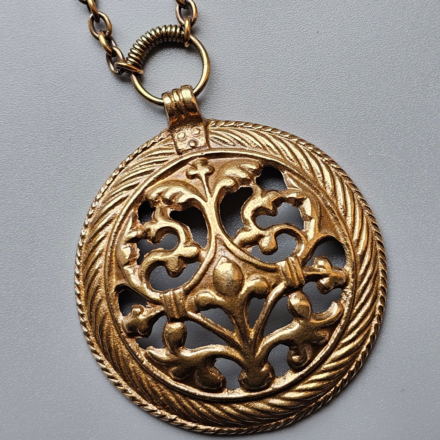 Ornate gold-toned pendant with intricate floral filigree design on a chain.
