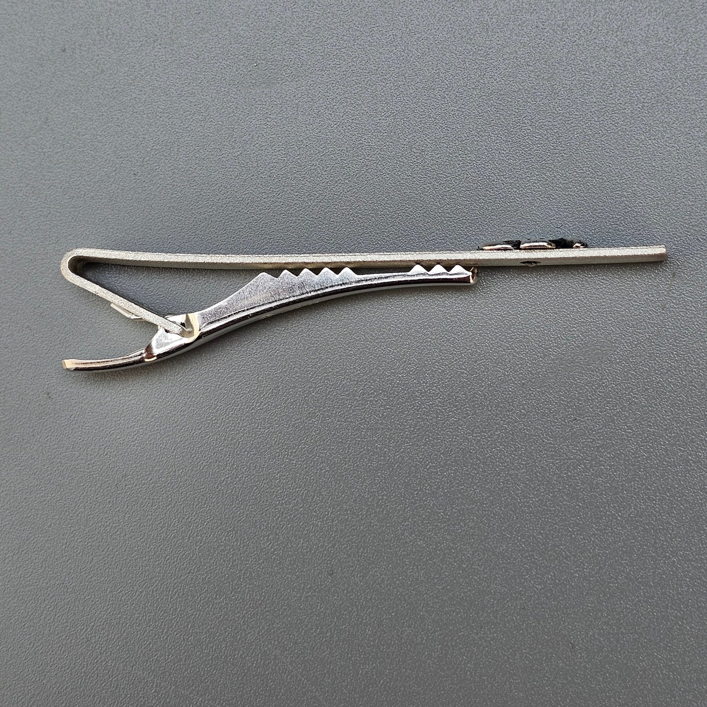 Metal hair clip with a serrated edge and spring-loaded mechanism.