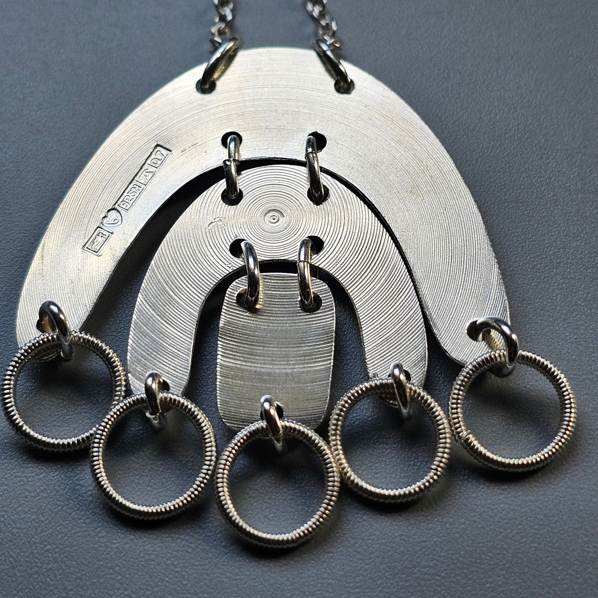 Metallic pendant necklace with concentric semicircular shapes and dangling rings.