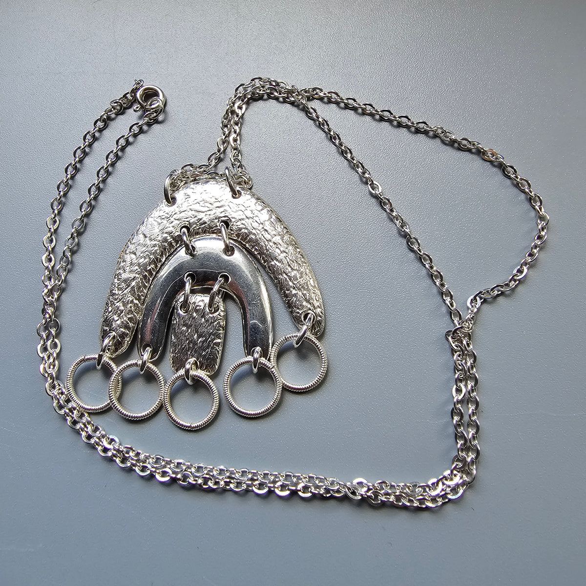 Silver pendant necklace featuring a stylized owl design with multiple rings.
