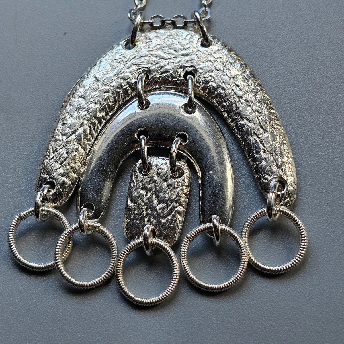 Ornate silver pendant necklace with multiple rings hanging from a crescent-shaped design.