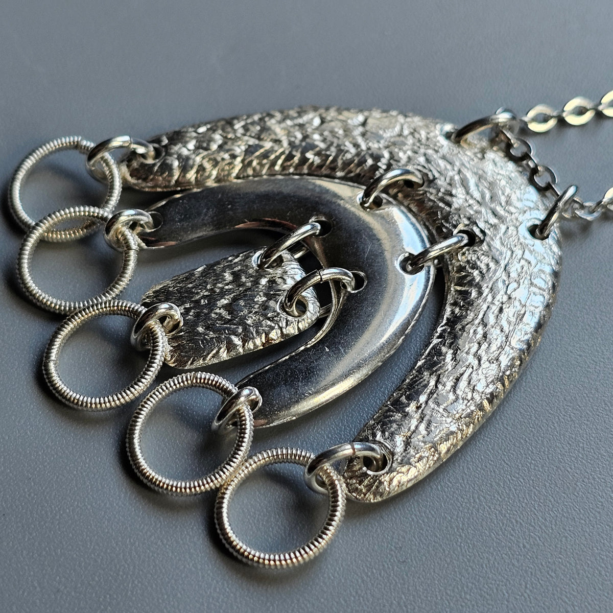 Ornate silver pendant necklace with crescent shapes and dangling rings.