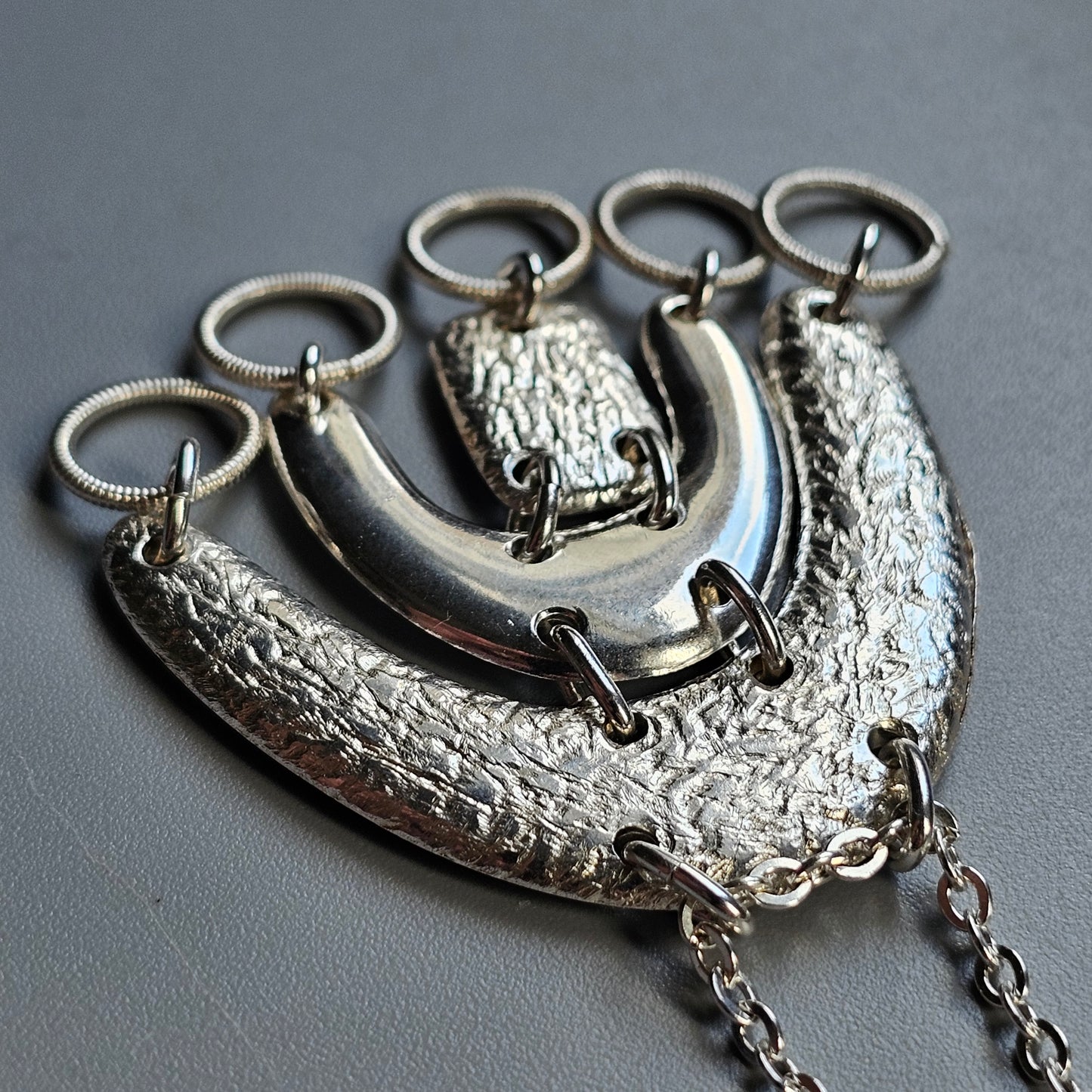 Silver-toned metal necklace with curved pendant and multiple rings attached.