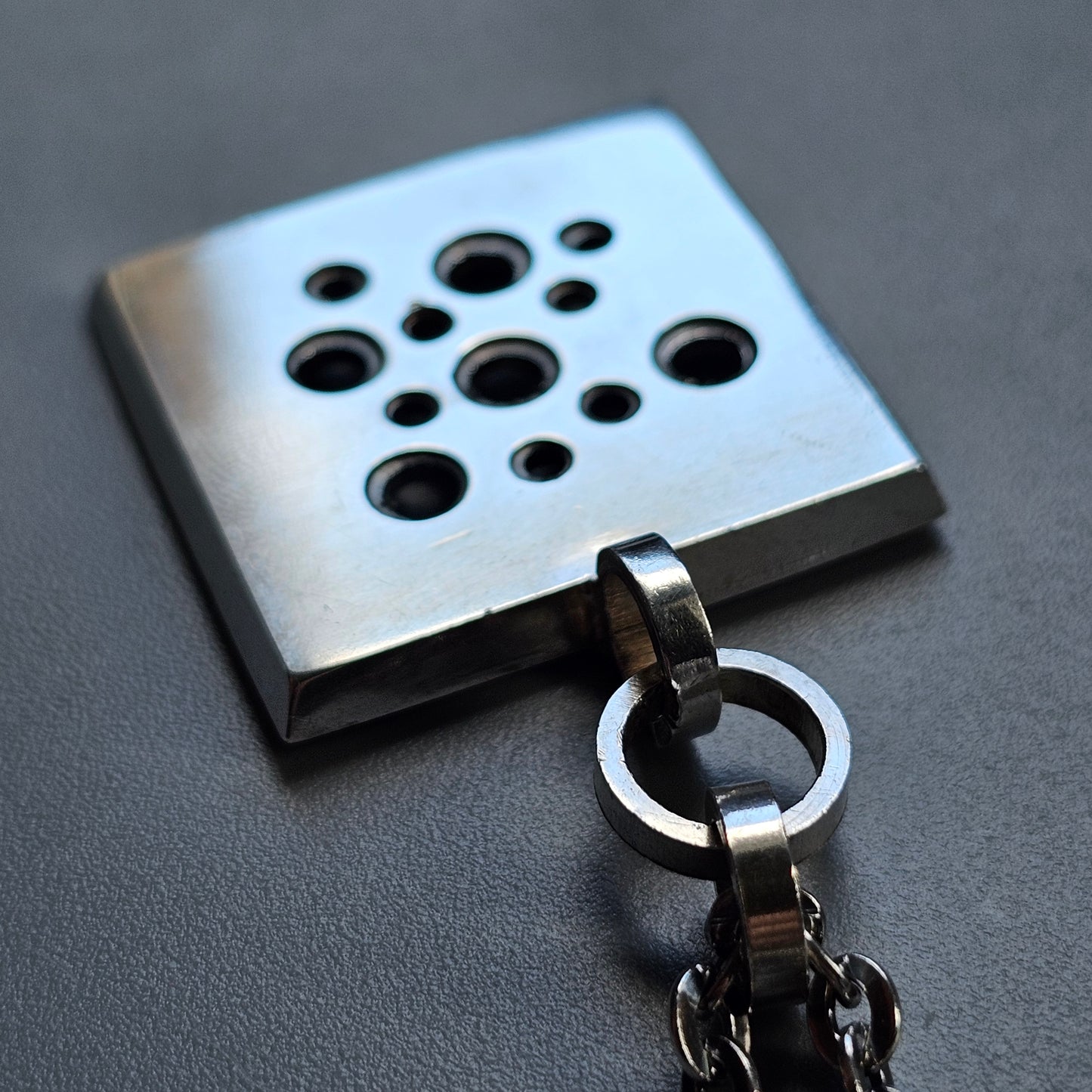 Metal keychain with a square pendant featuring multiple circular holes of varying sizes.