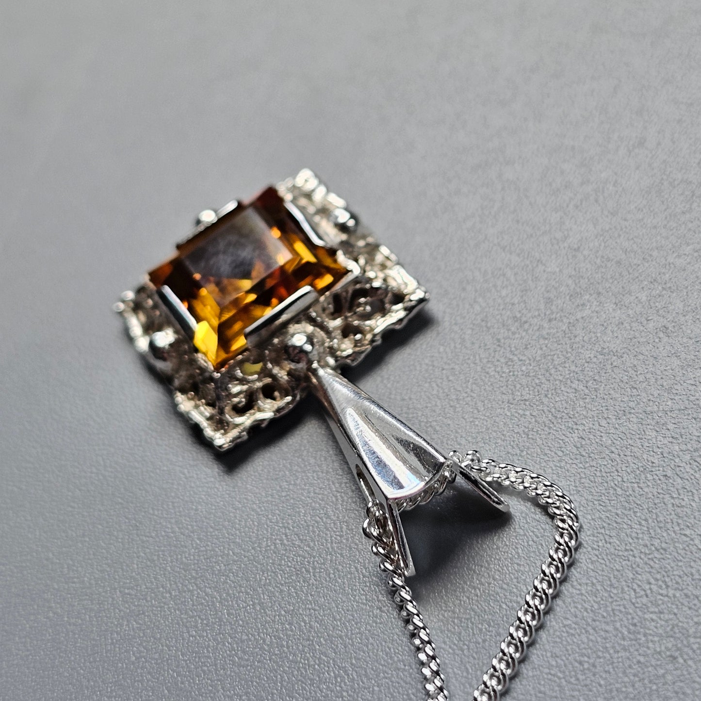 Ornate silver pendant featuring a square-cut amber-colored gemstone.