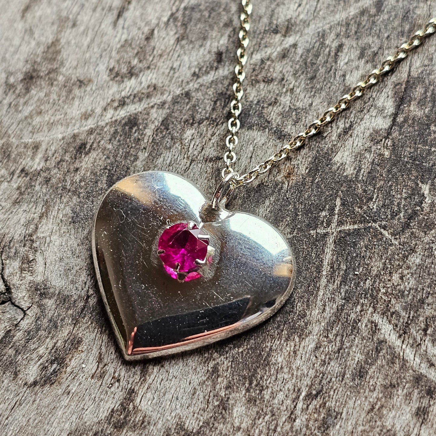 Heart-shaped silver pendant with a pink gemstone, hanging on a chain.