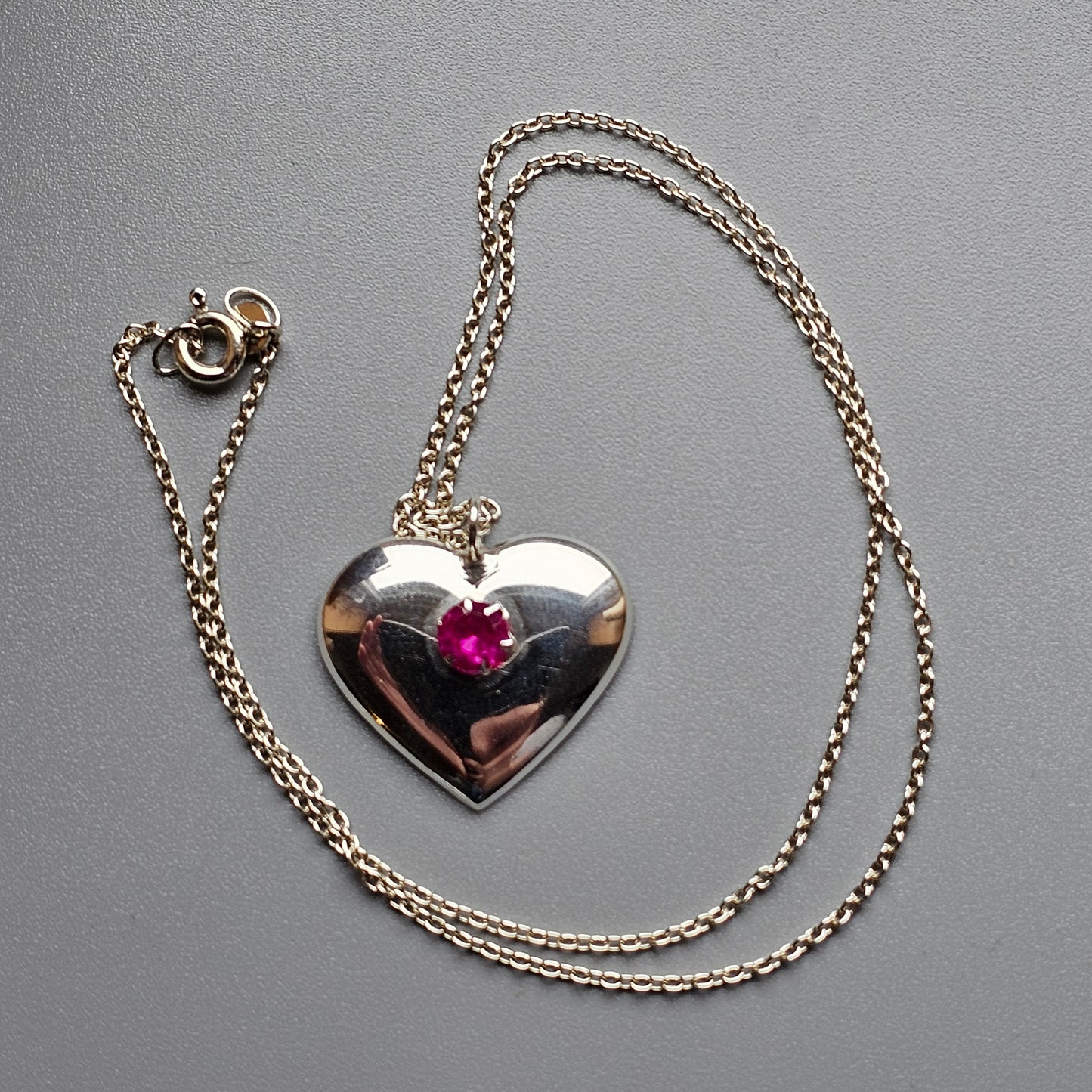 Heart-shaped silver pendant with a pink gemstone, attached to a delicate chain necklace.