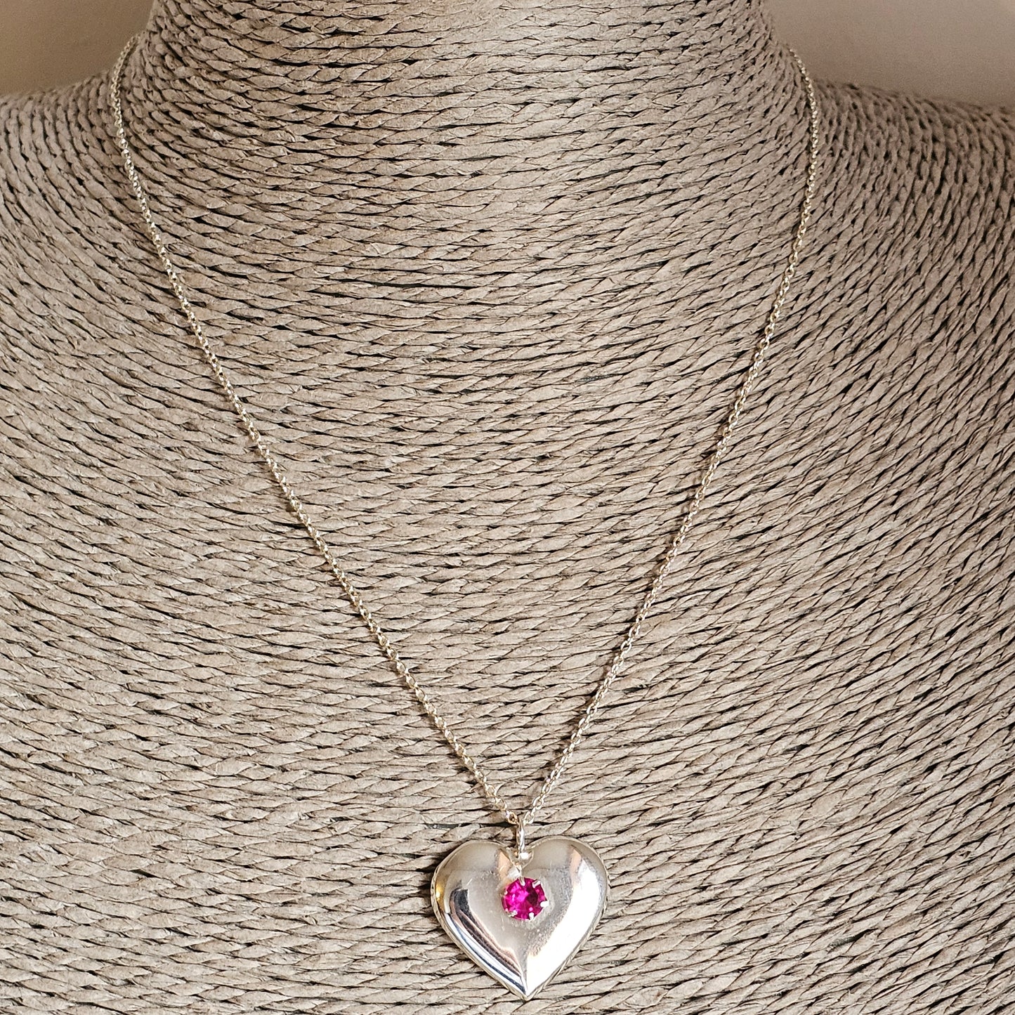 Heart-shaped silver pendant necklace with a pink gemstone accent.