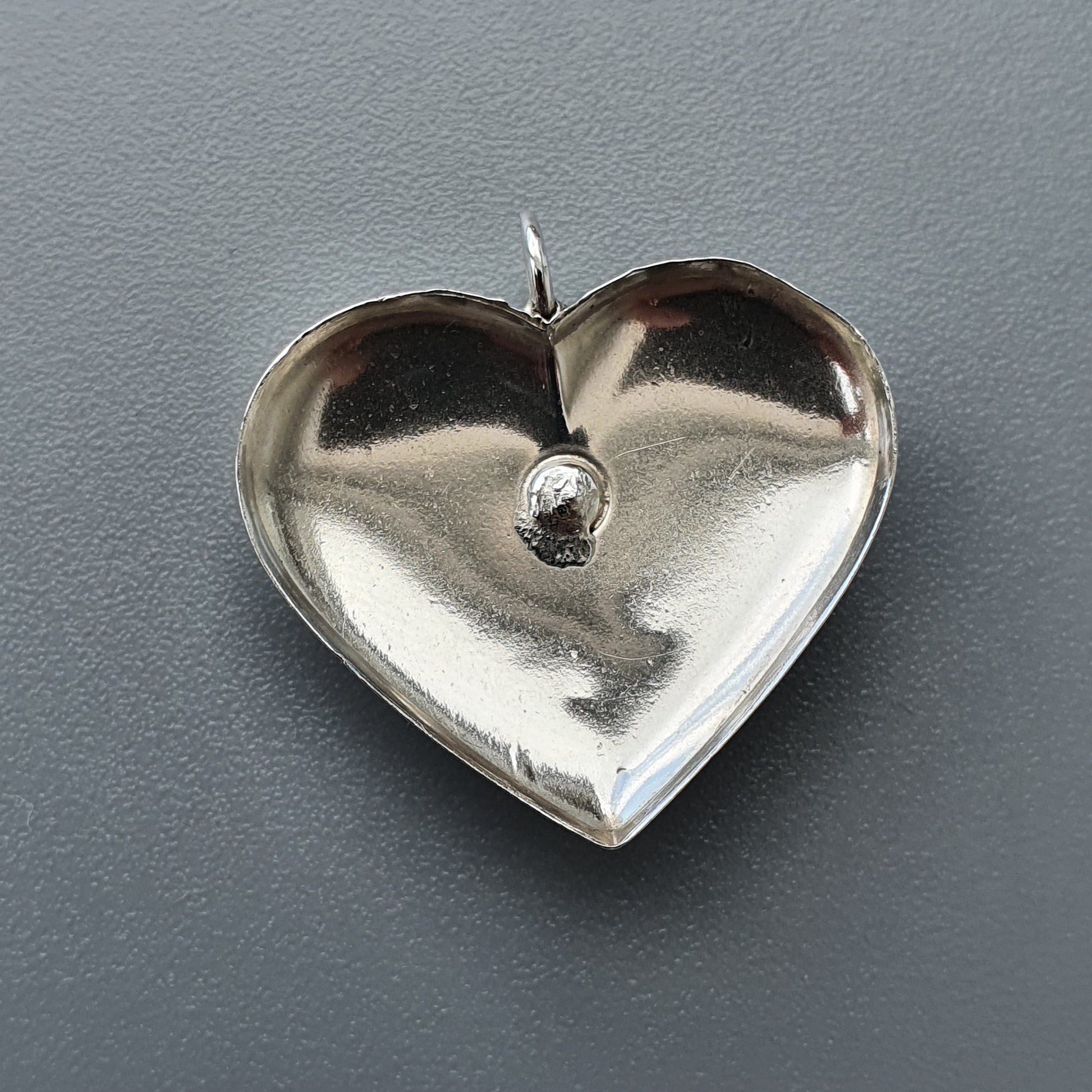 Silver heart-shaped pendant with a small indentation in the center.