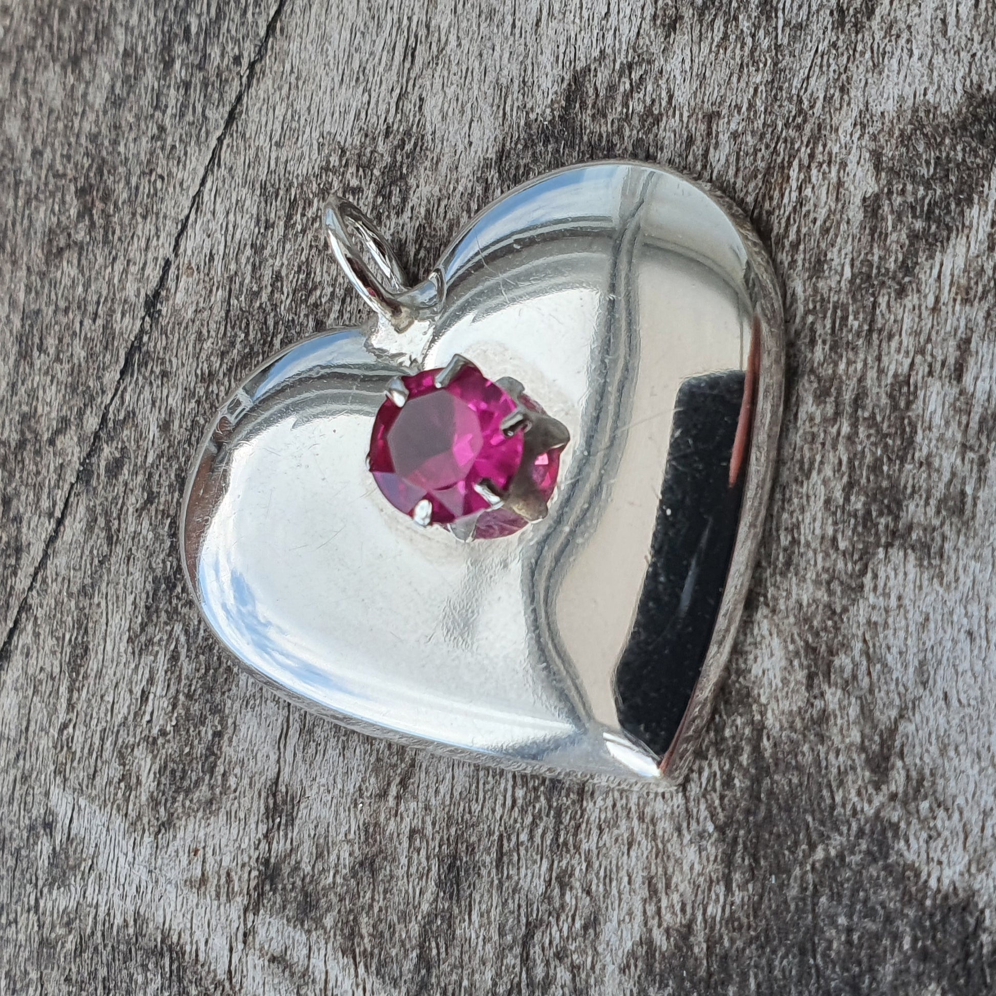 Silver heart-shaped pendant with a pink gemstone.