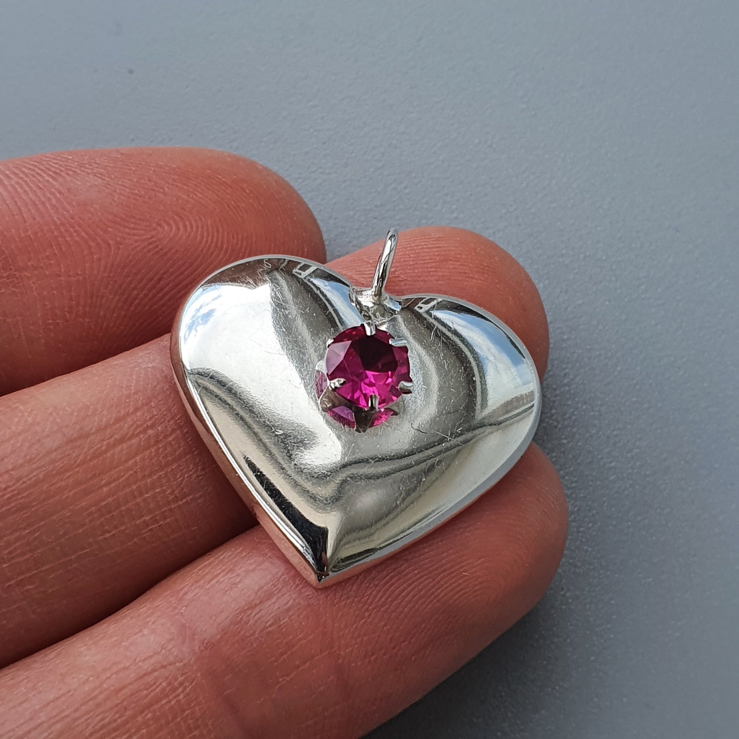 Silver heart-shaped pendant with a pink gemstone in the center.