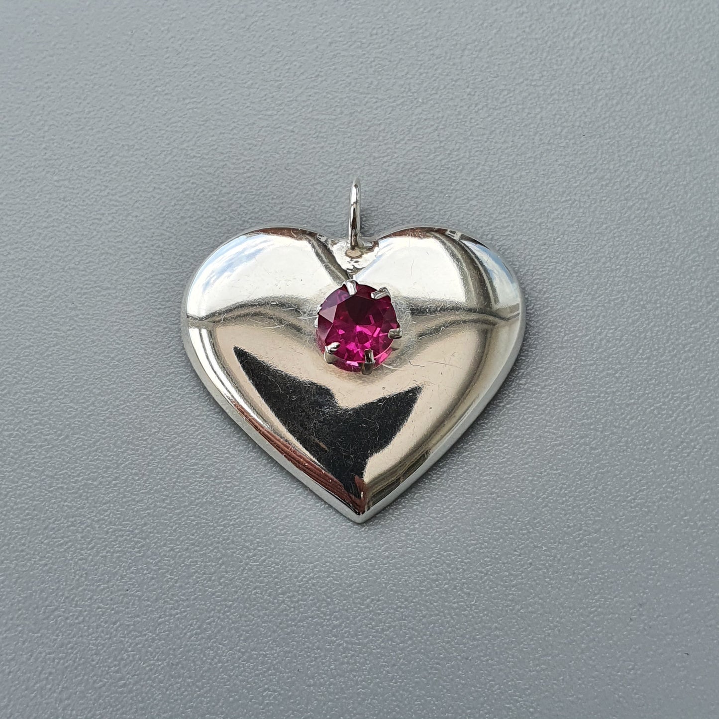 Heart-shaped silver pendant with a pink gemstone in the center.