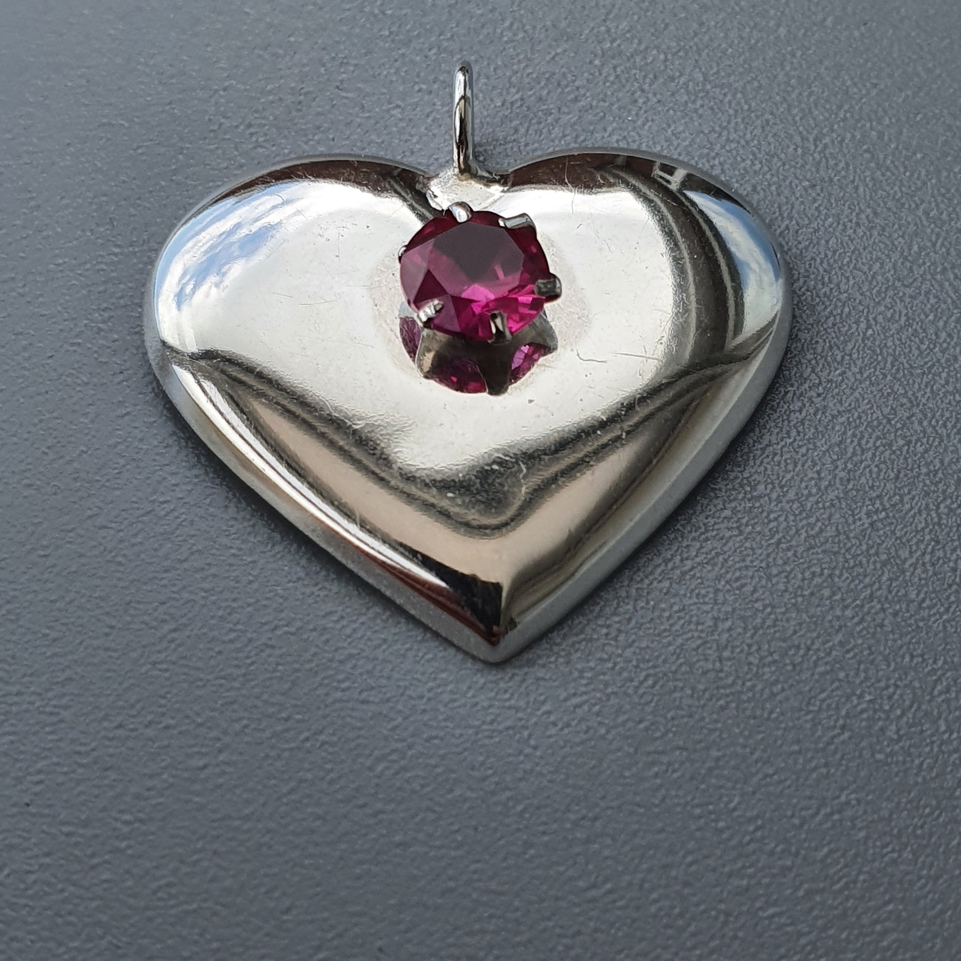 Heart-shaped silver pendant with a pink gemstone in the center.