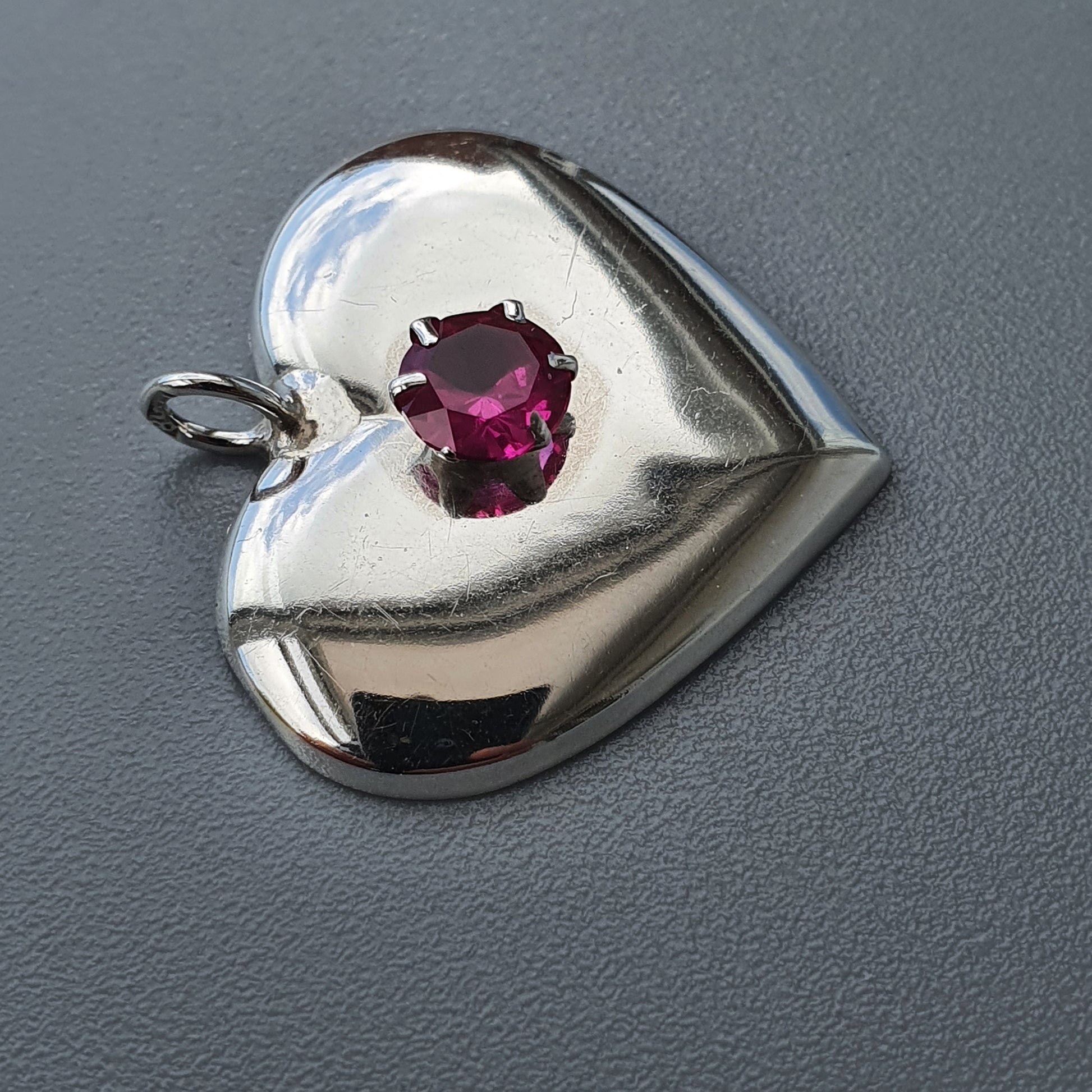 Heart-shaped silver pendant with a pink gemstone.