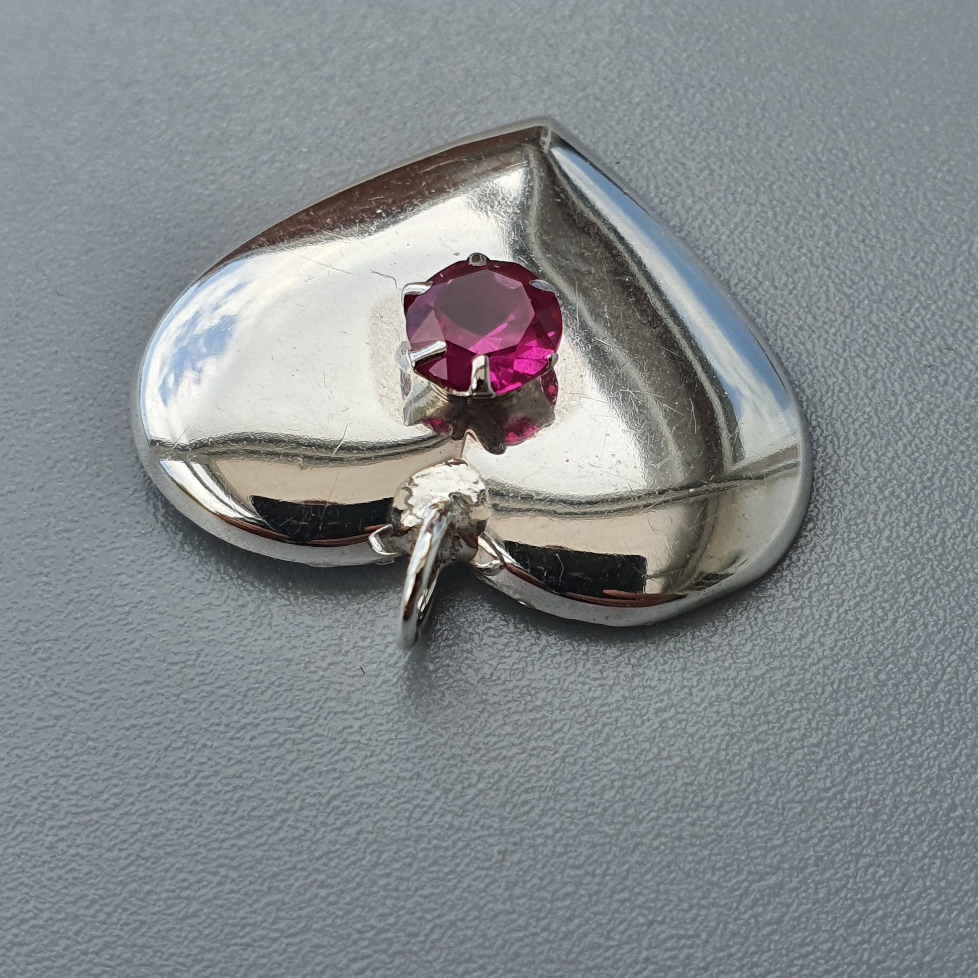 Heart-shaped silver pendant with a pink gemstone.