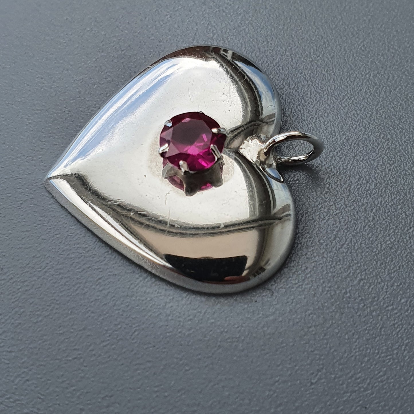 Heart-shaped silver pendant with a pink gemstone in the center.