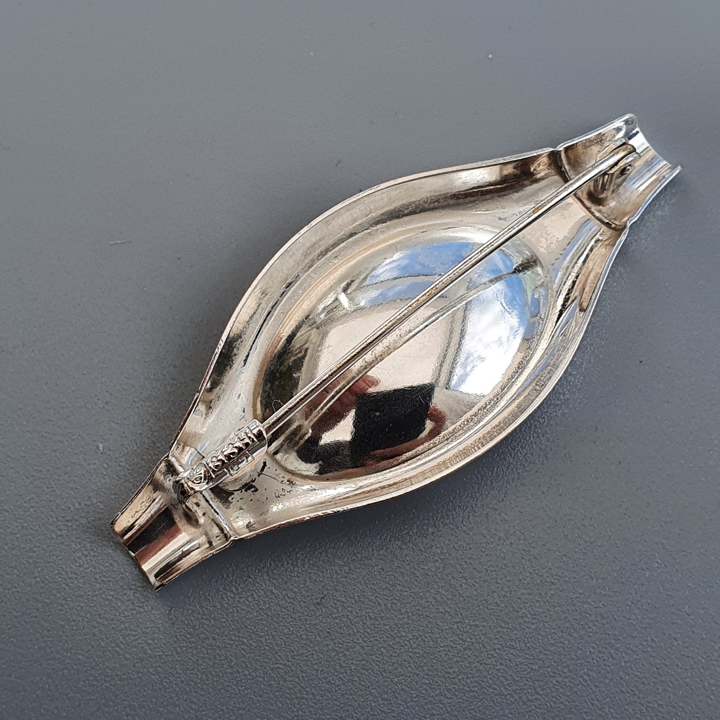 Silver-colored, eye-shaped decorative object with a reflective surface and pointed ends.