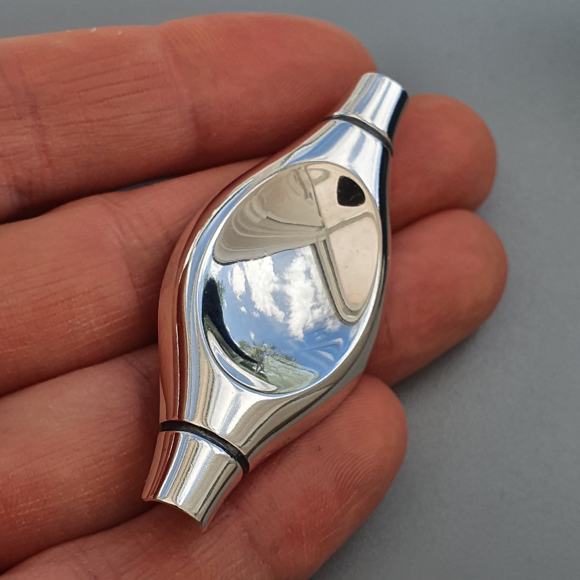 Shiny silver-colored metal whistle held between fingers.