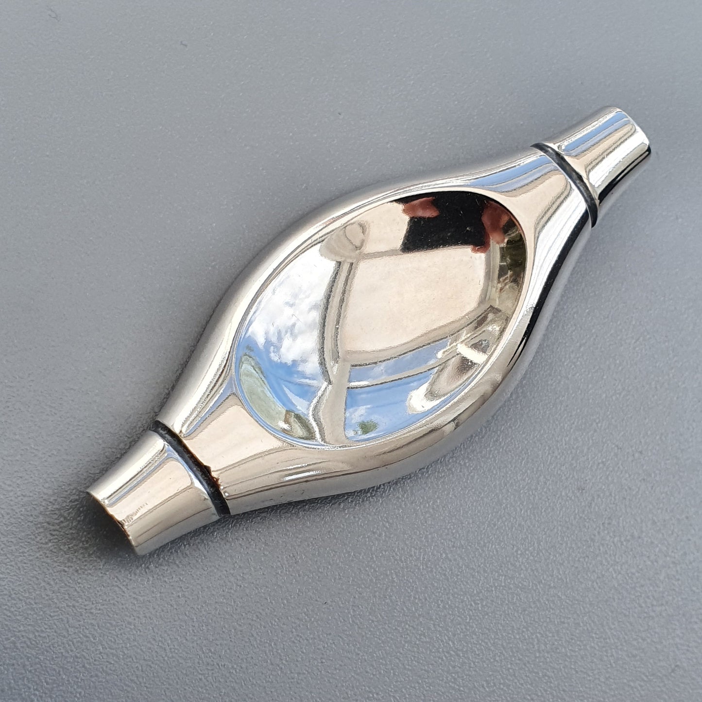 Shiny metallic object with an oval-shaped bulge containing a clear liquid or glass element.