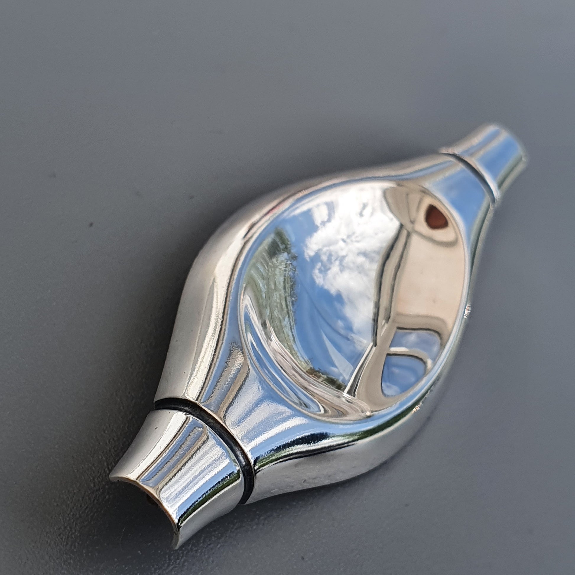 Shiny metallic whistle with a curved, teardrop-shaped body and a small hole near the mouthpiece.