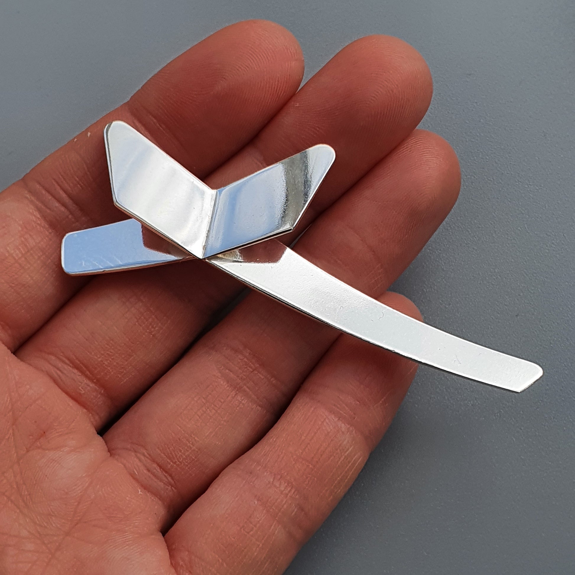 Small metal paper airplane or glider resting on an open palm.