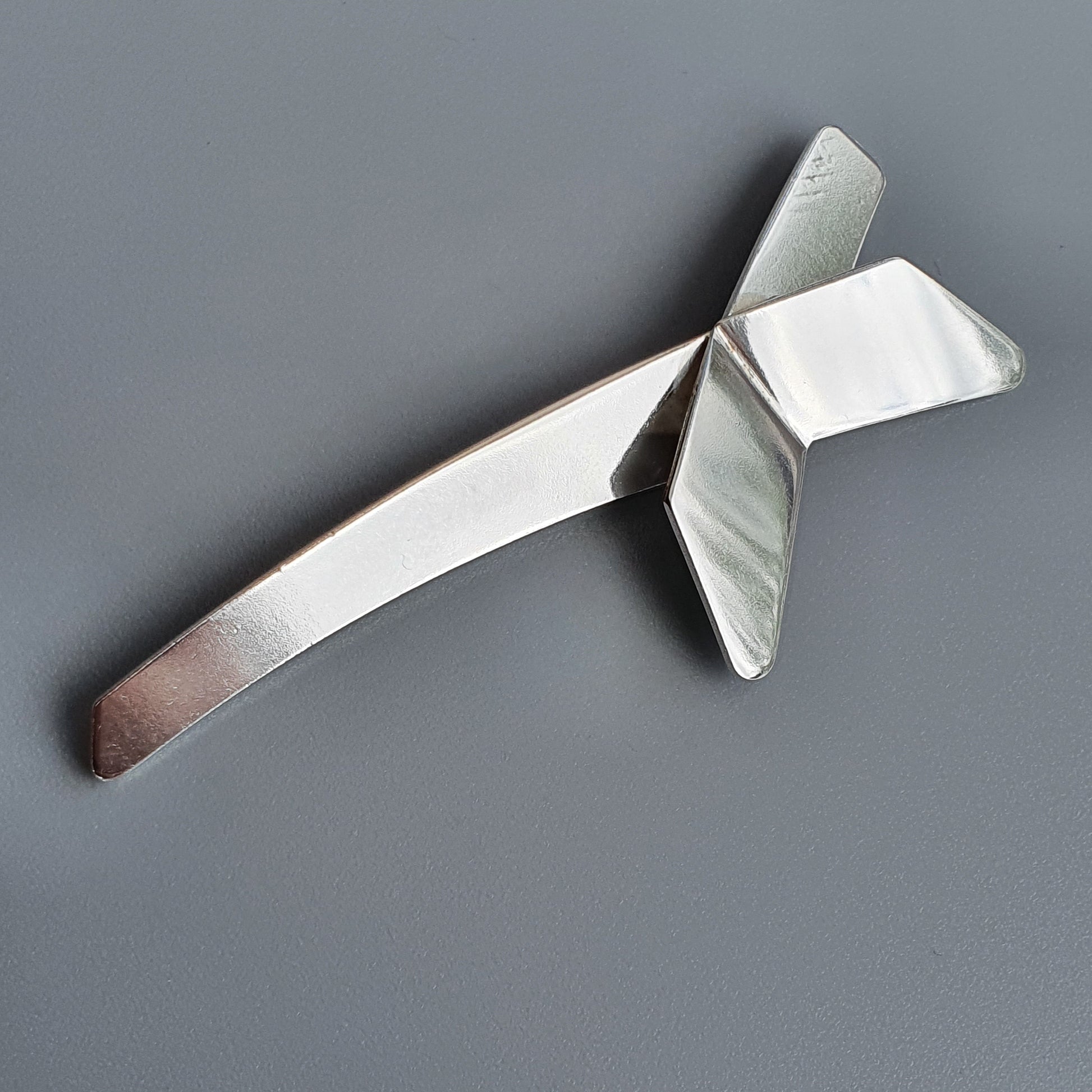 Metallic cross-shaped object with a long handle and angled wings.