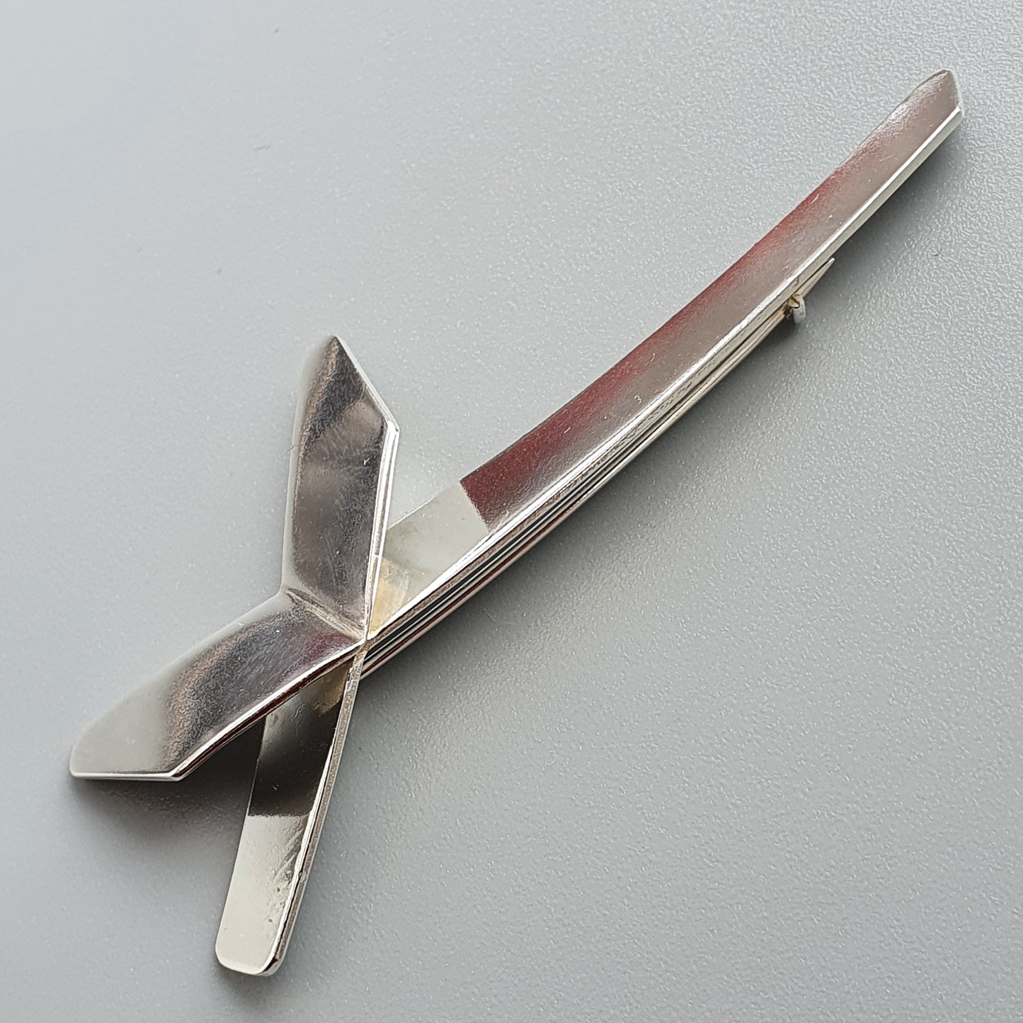 Silver-colored metal tie clip with a stylized ribbon or bow design.