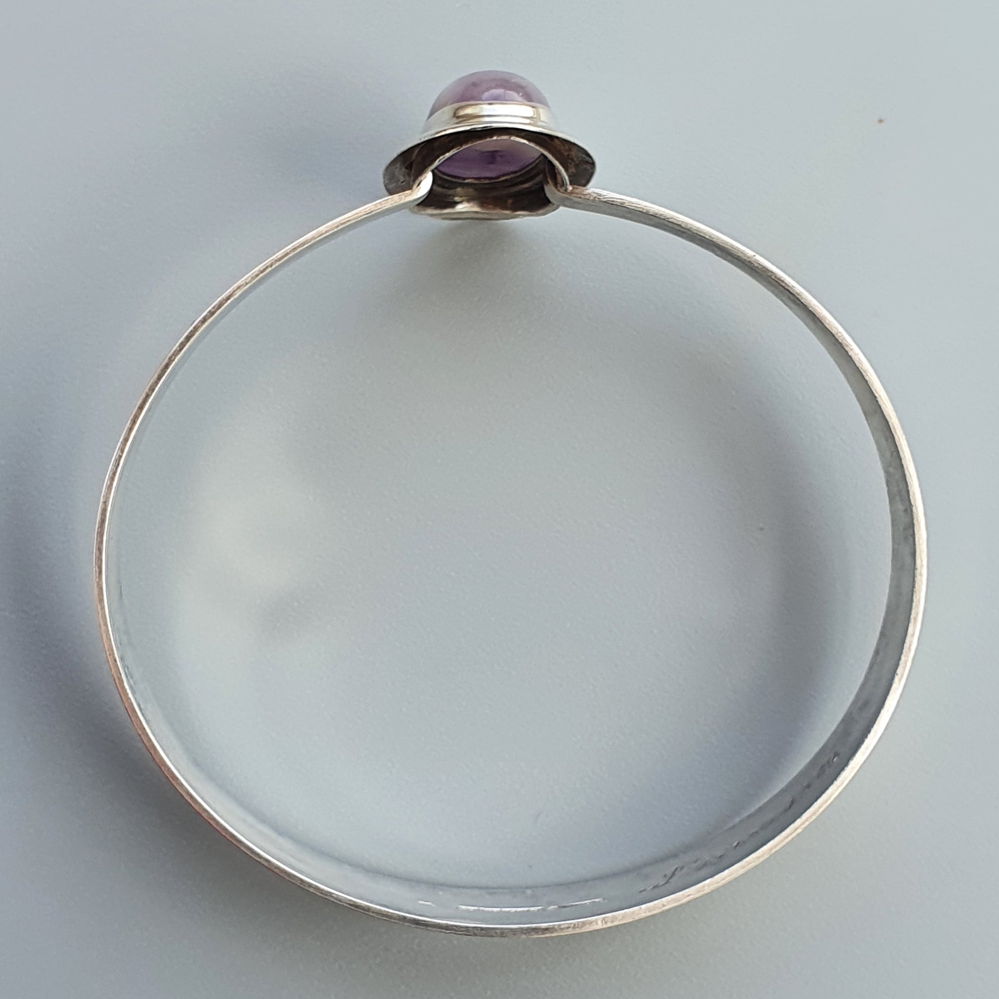 Silver bangle bracelet with a purple gemstone setting.