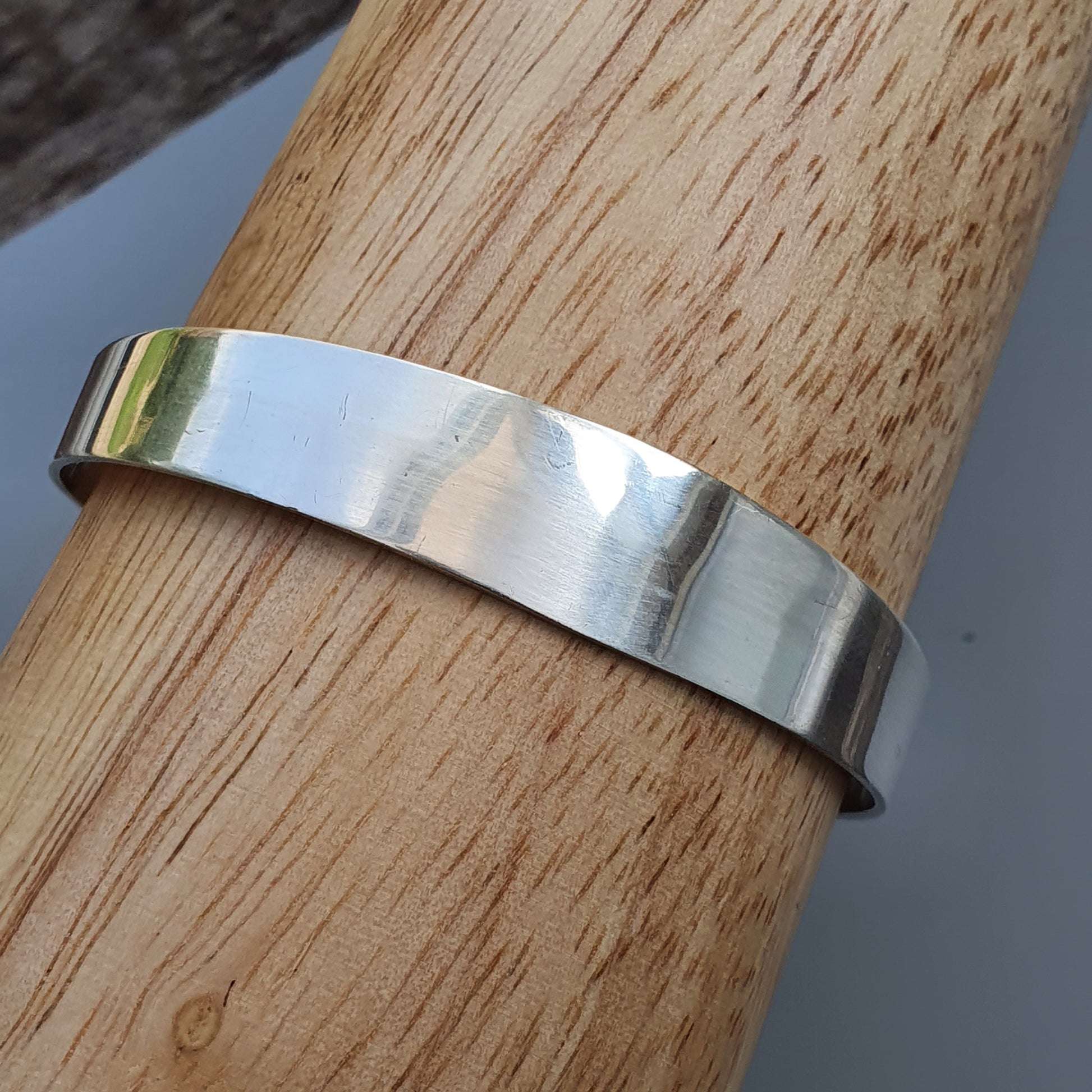 Silver metal cuff bracelet wrapped around a wooden surface.