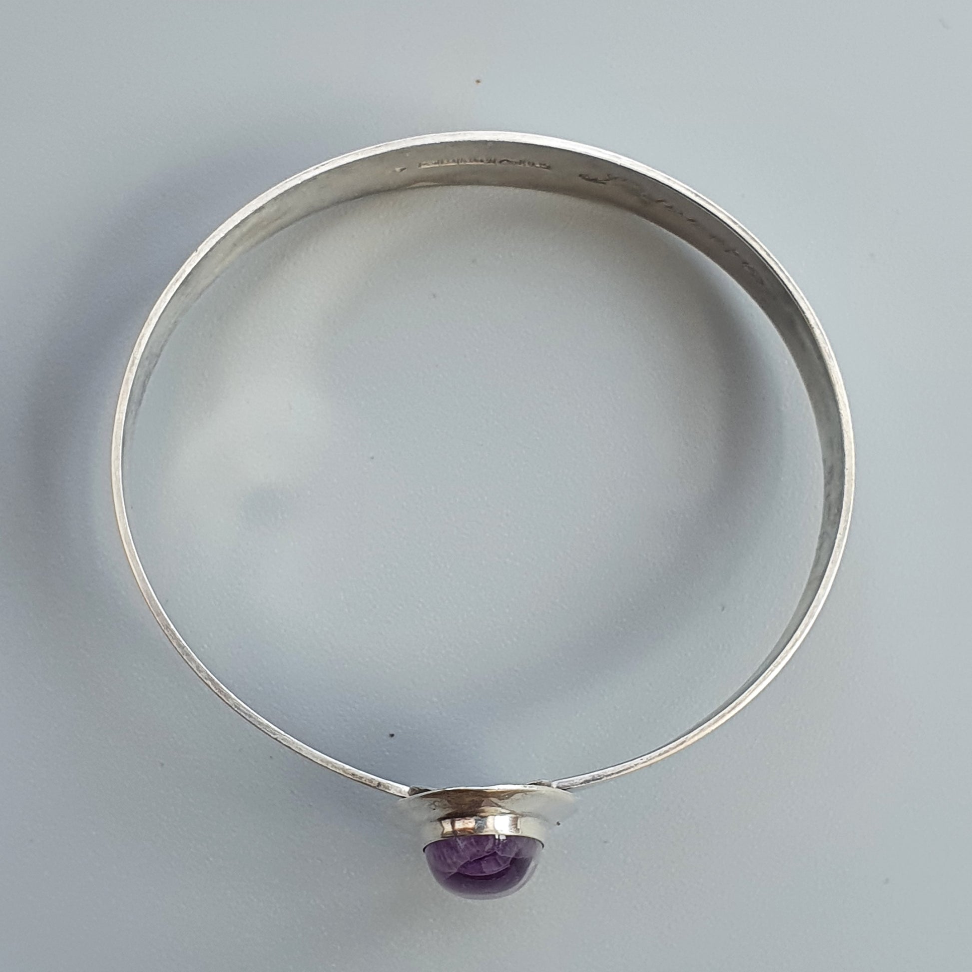 Silver bangle bracelet with a small purple gemstone pendant.