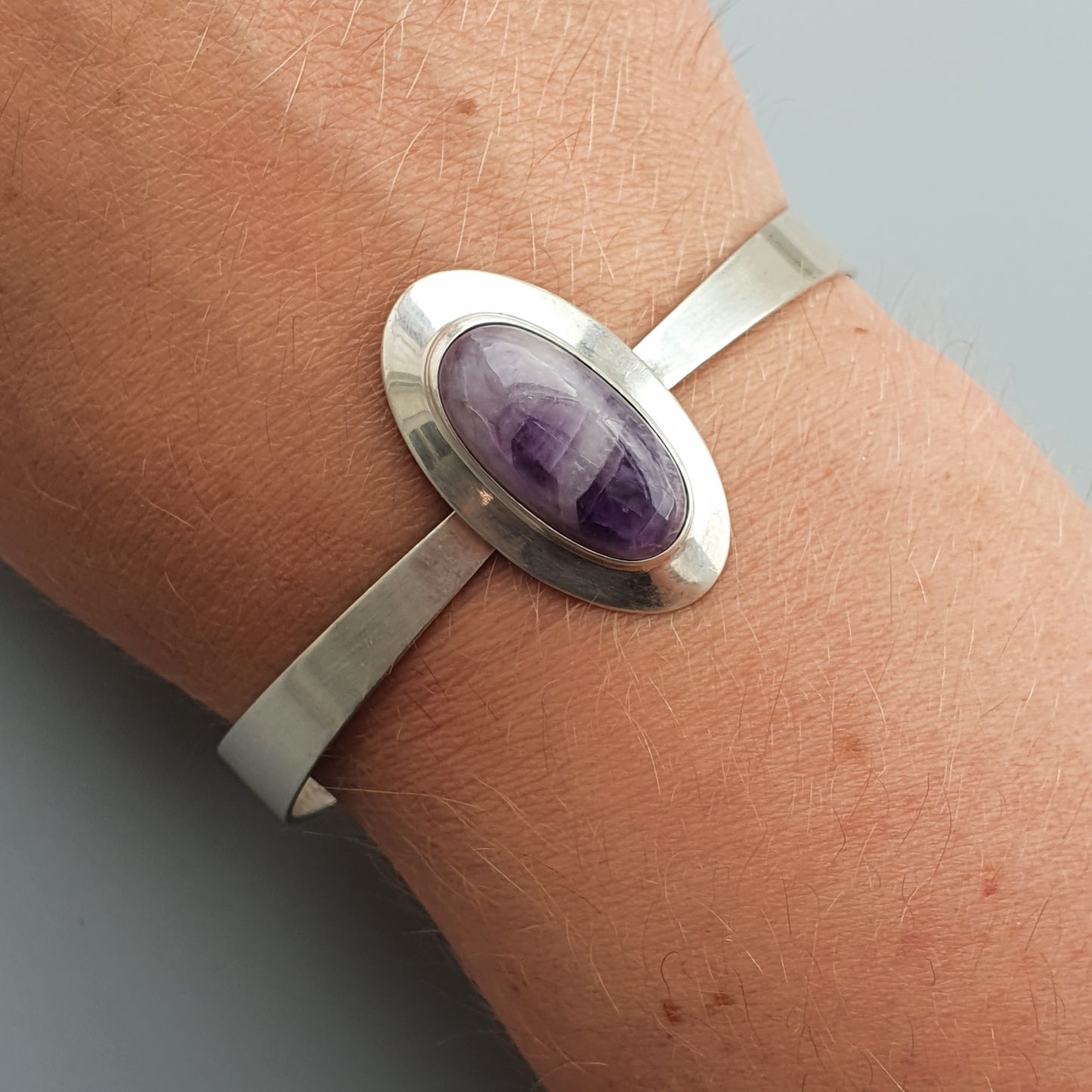 Silver bracelet featuring an oval purple gemstone.