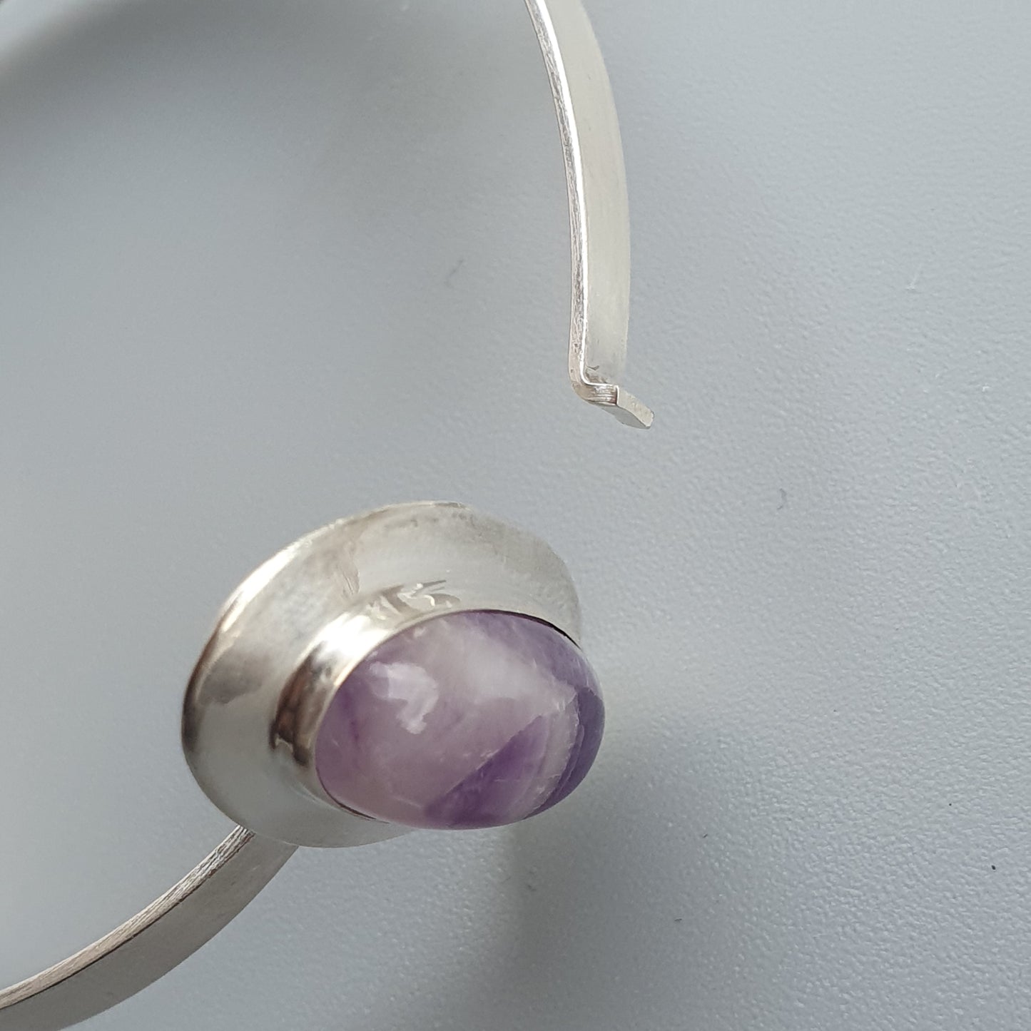 Silver bracelet or bangle with a purple gemstone setting.