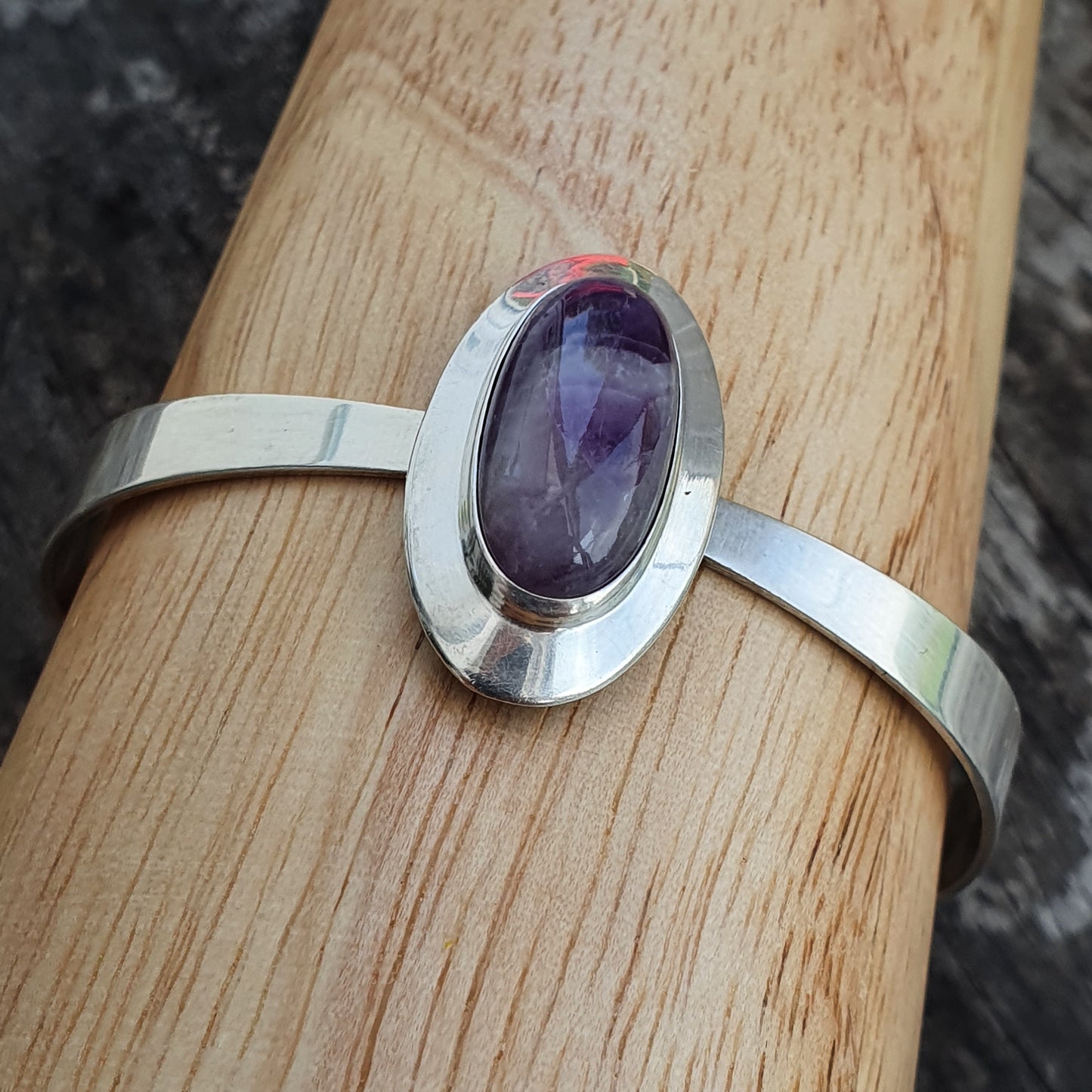 Silver bracelet featuring an oval purple gemstone.