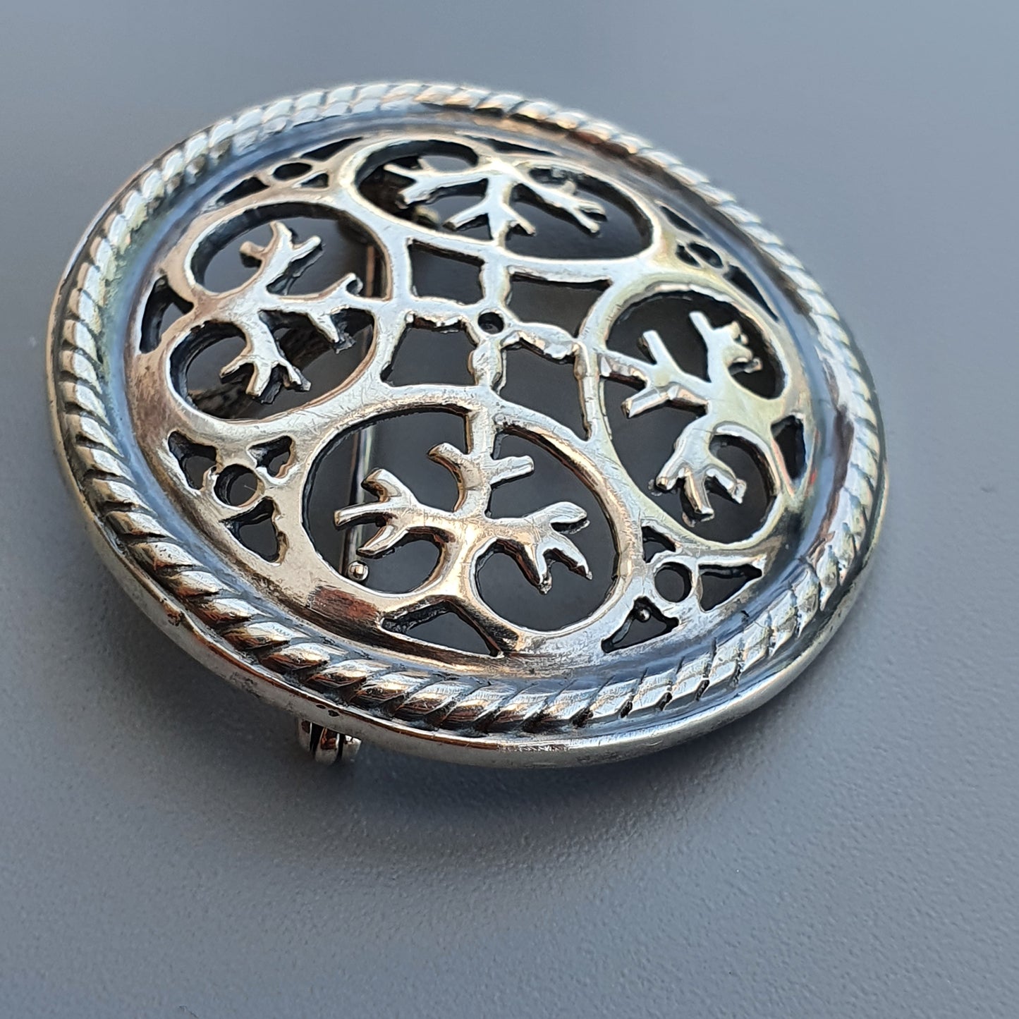 Ornate silver brooch with intricate bird-like designs in a circular pattern.