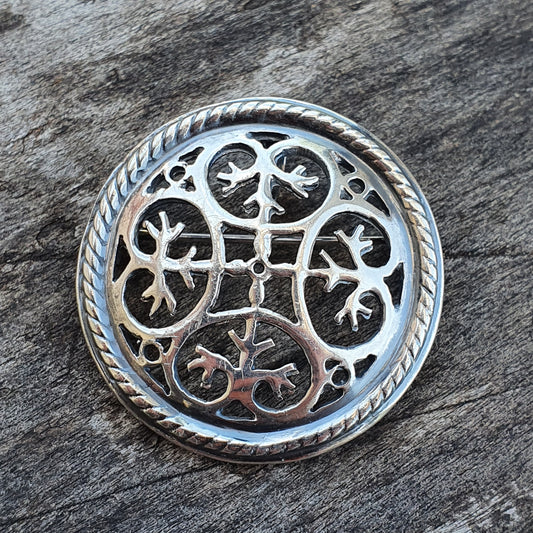 Ornate silver brooch or pendant with intricate Celtic-style knotwork design.