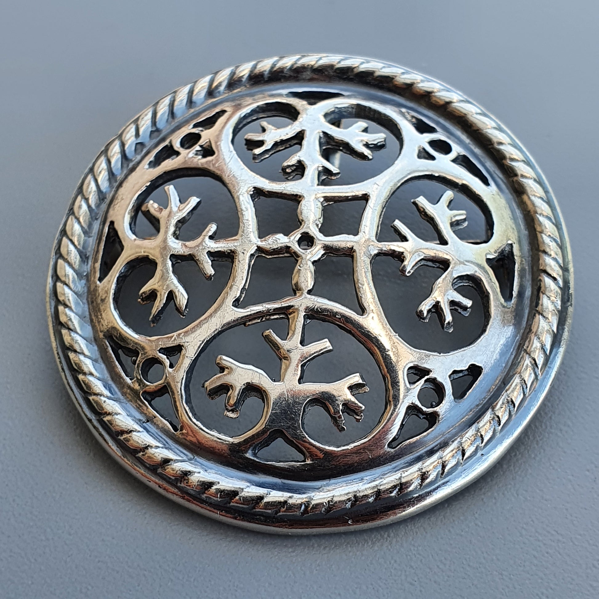 Ornate silver brooch with intricate Celtic-inspired design featuring swirling patterns and animal motifs.