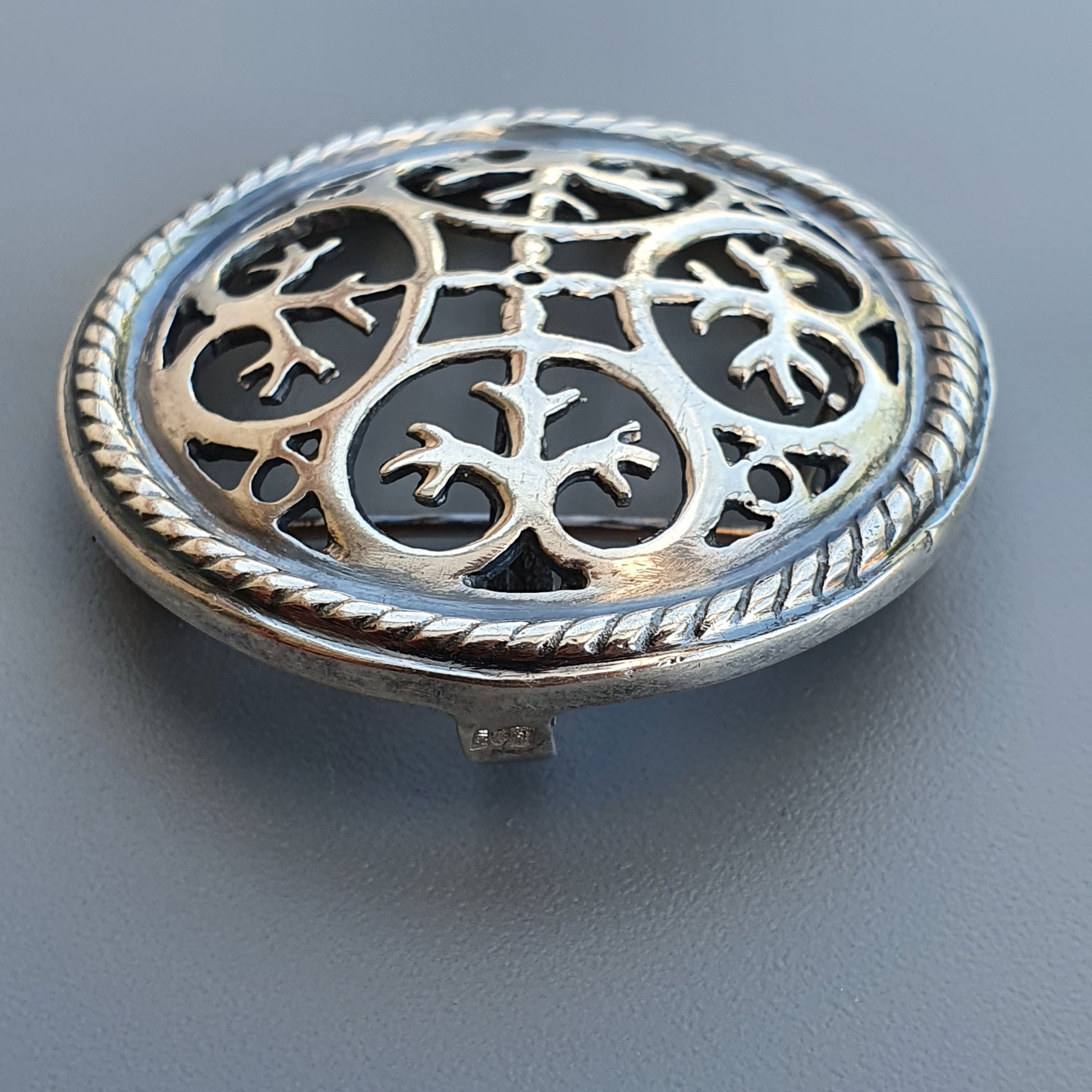 Ornate silver brooch or pendant with intricate cutout floral design and rope-like border.