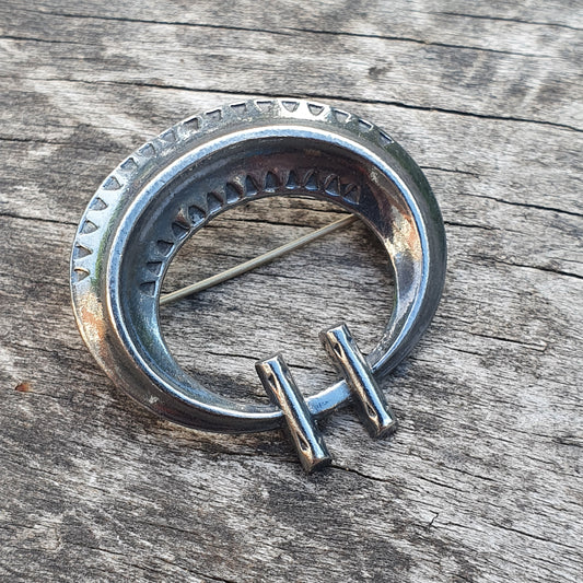 Circular metal brooch or pin with decorative ridged edges and a protruding clasp.