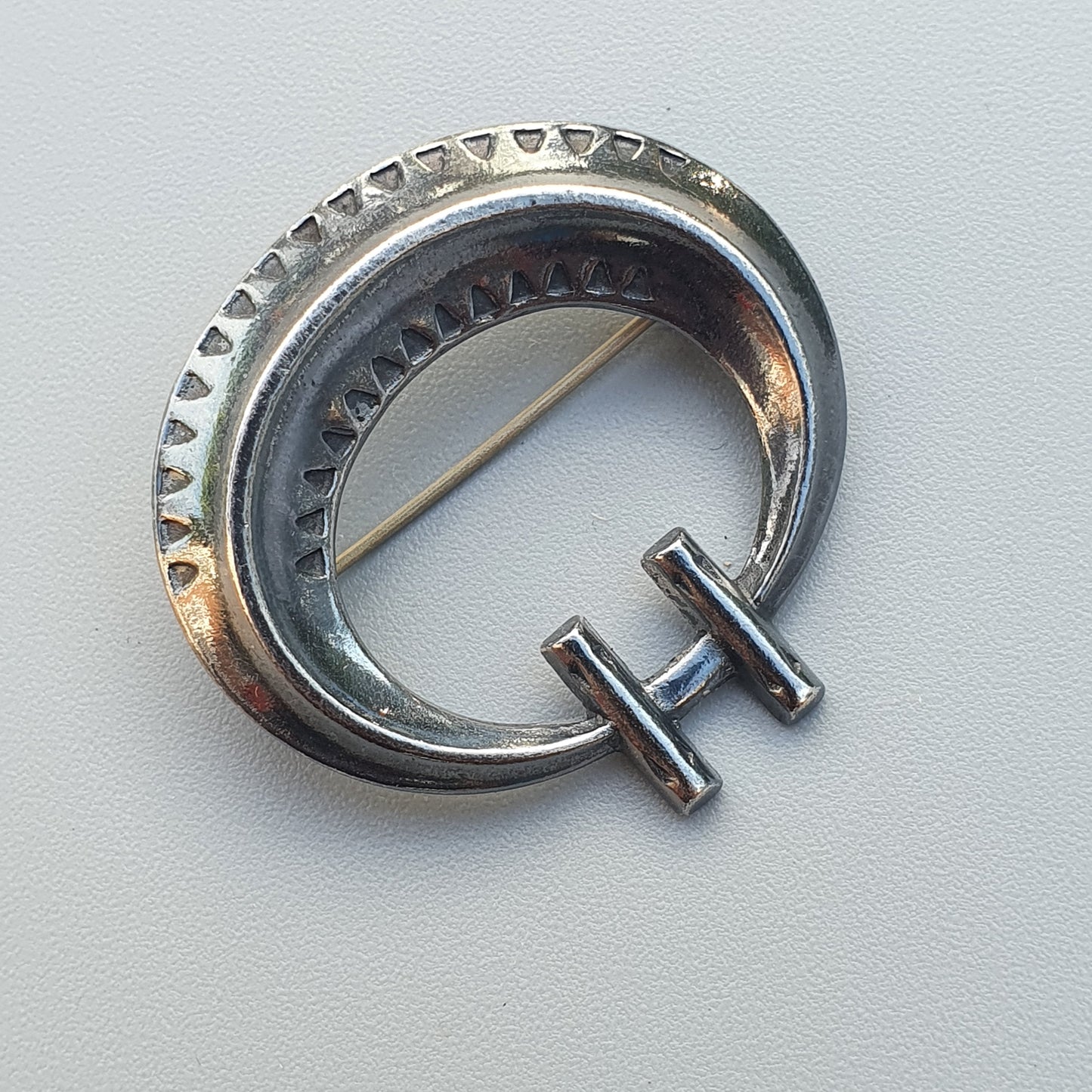 Silver crescent-shaped brooch or pin with decorative ridges and a protruding bar.